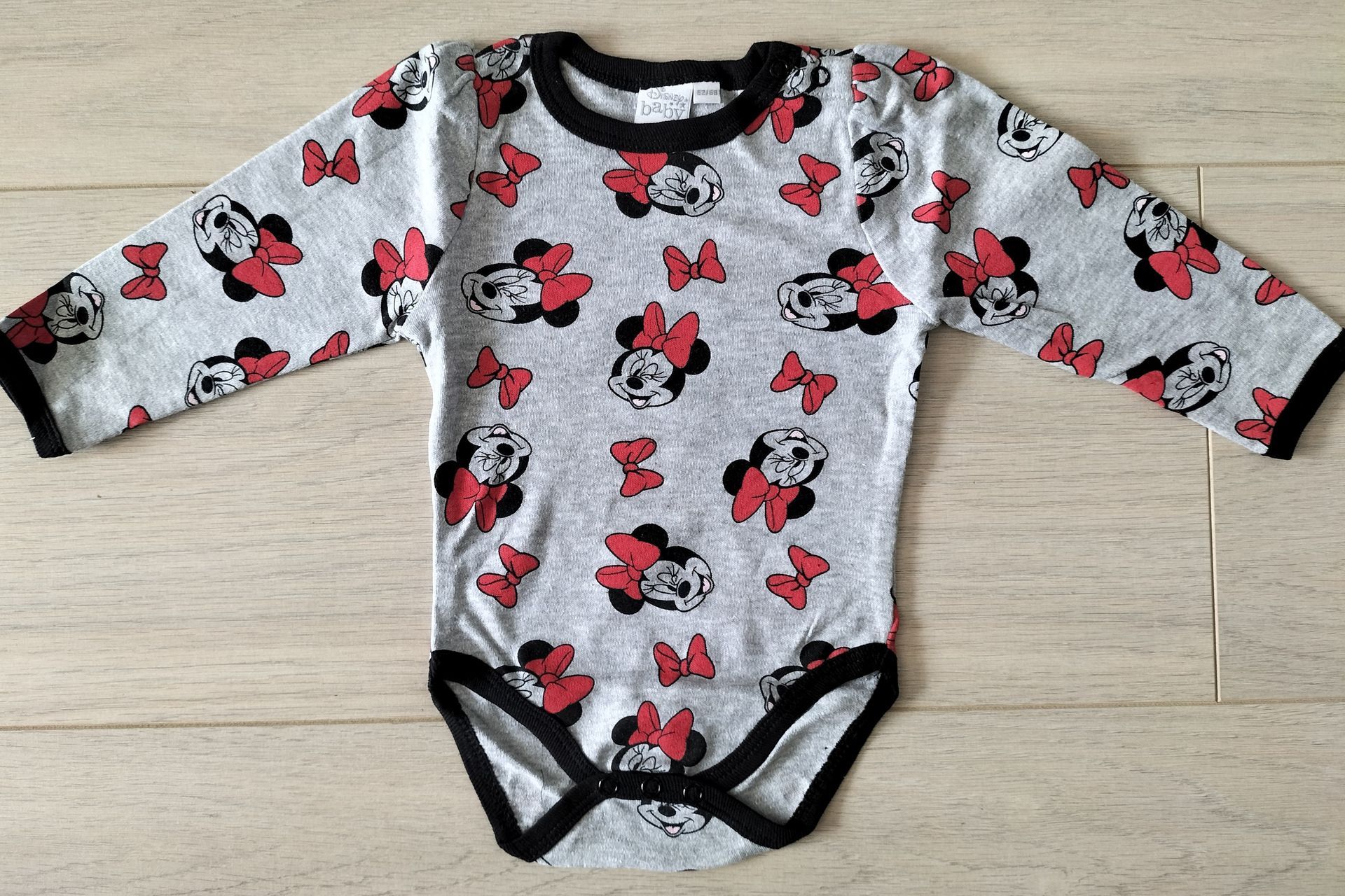 Grijze babyromper met Minnie Mouse-print, zwarte bies en lange mouwen.
