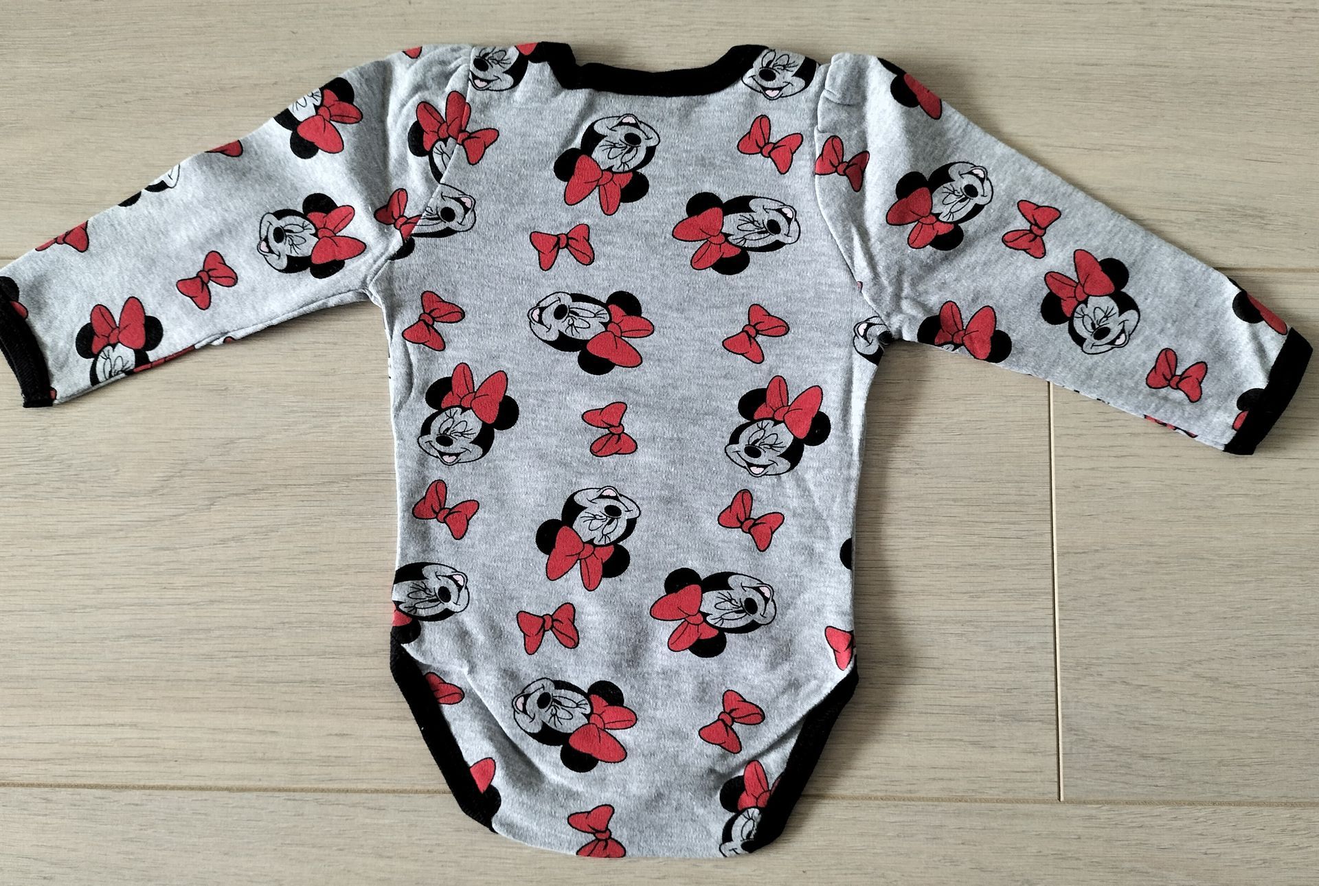Grijze babyromper met Minnie Mouse-print, zwarte bies en lange mouwen.