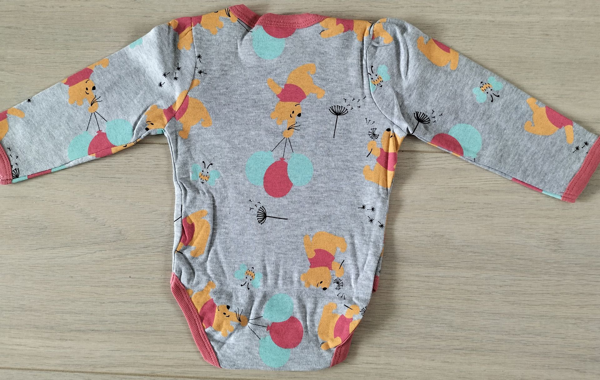 Grijze babyromper met bloemenprint en rode bies.