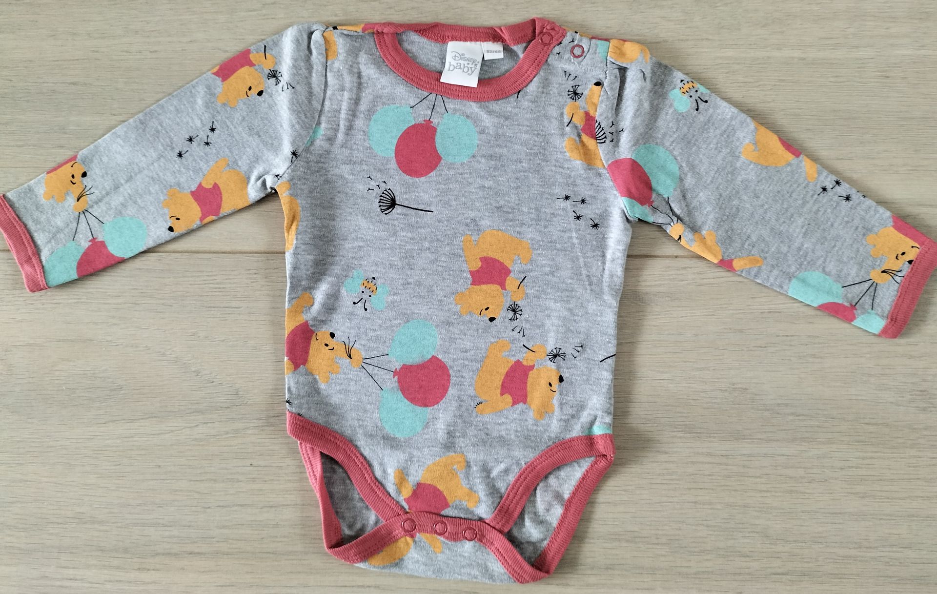 Grijze babyromper met bloemenprint en rode bies.