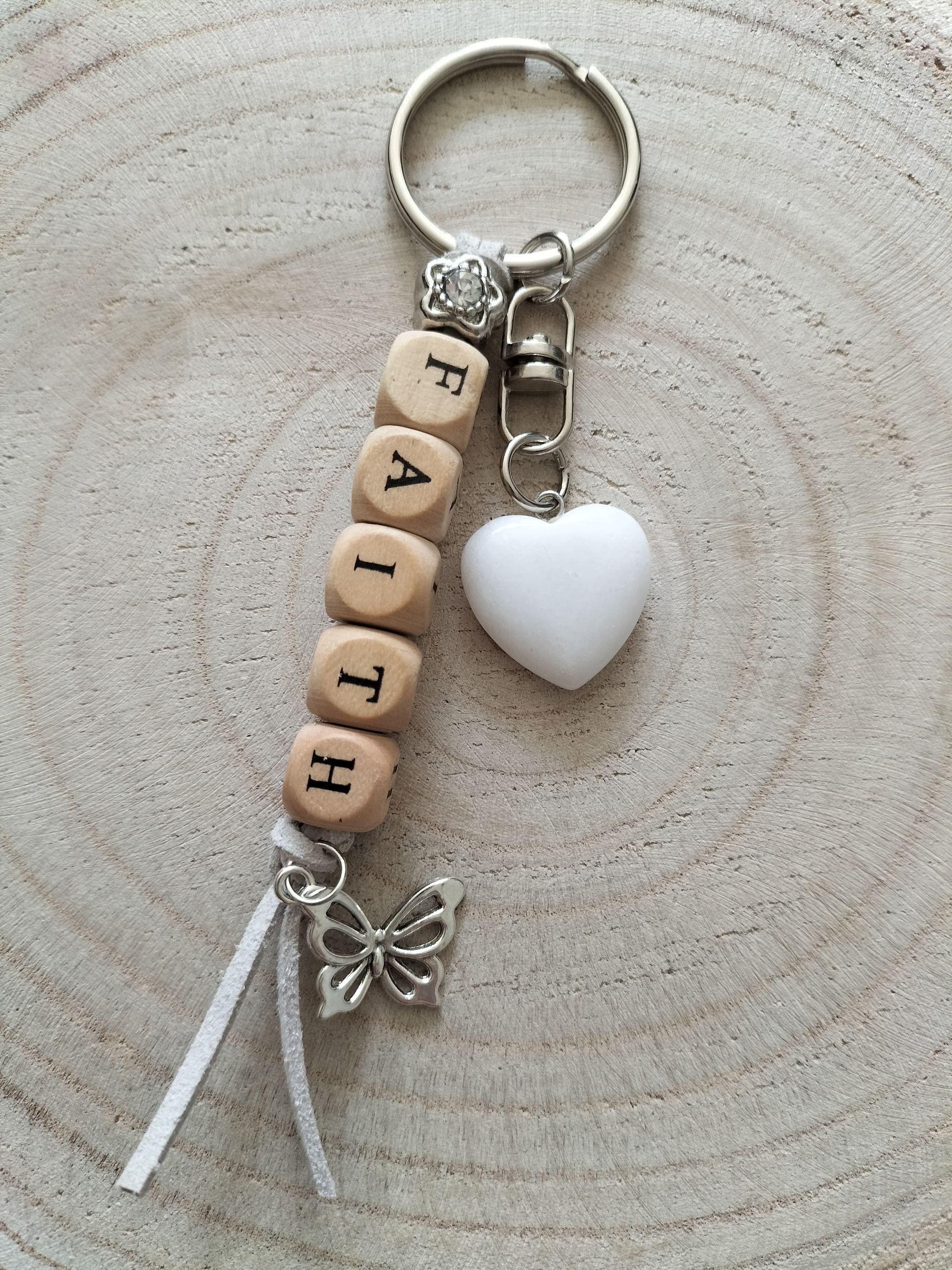 Sleutelhanger met houten kralen die het woord "FAITH" vormen en een witte jade hartje en vlinder bedeltje.