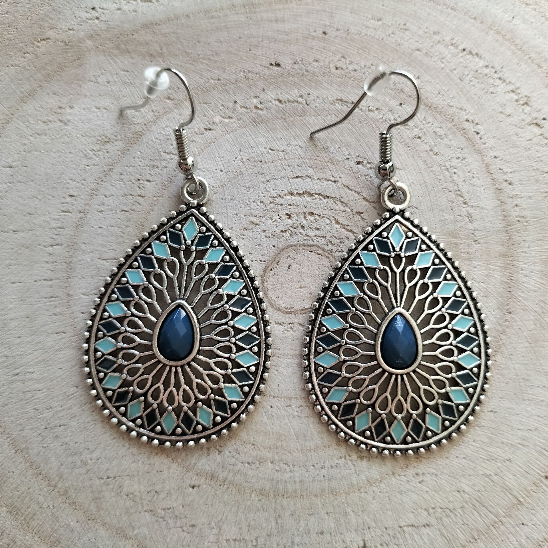 Een paar druppelvormige oorbellen, zilverkleurig, met blauwe en turquoise emaille inleg.