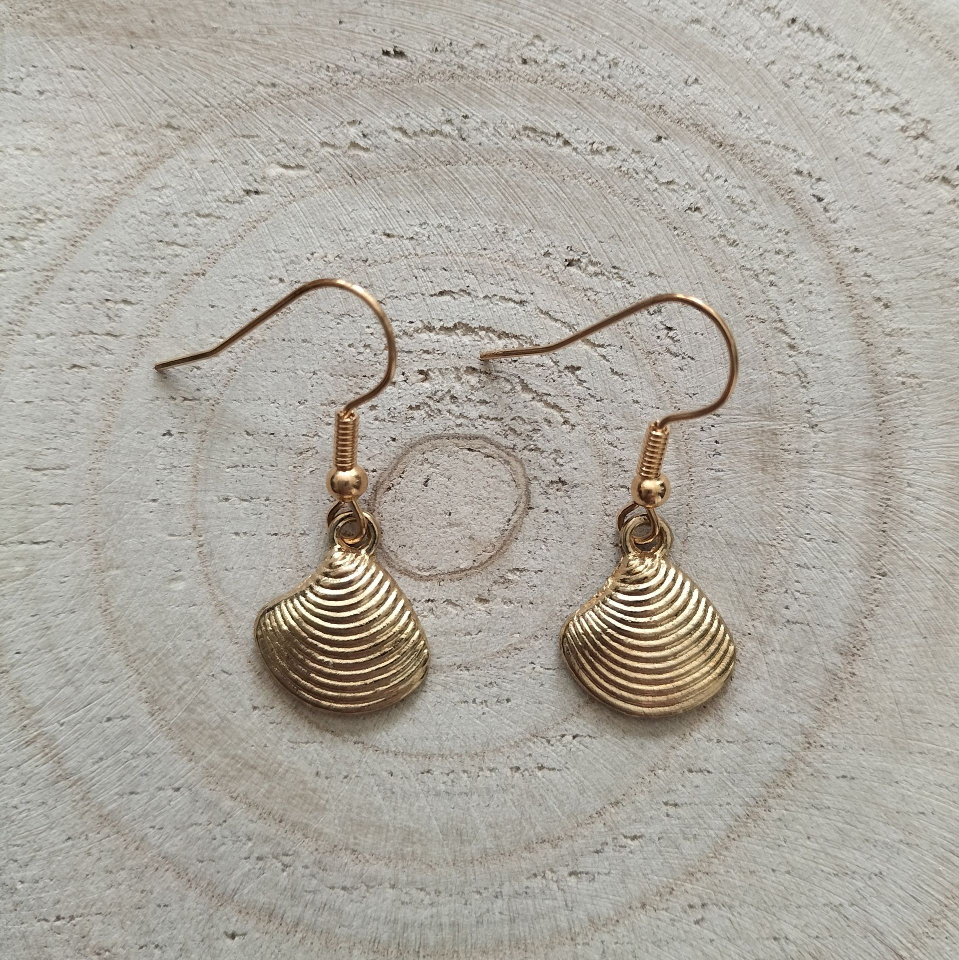 Gouden oorbellen in de vorm van schelpen op een houten achtergrond.