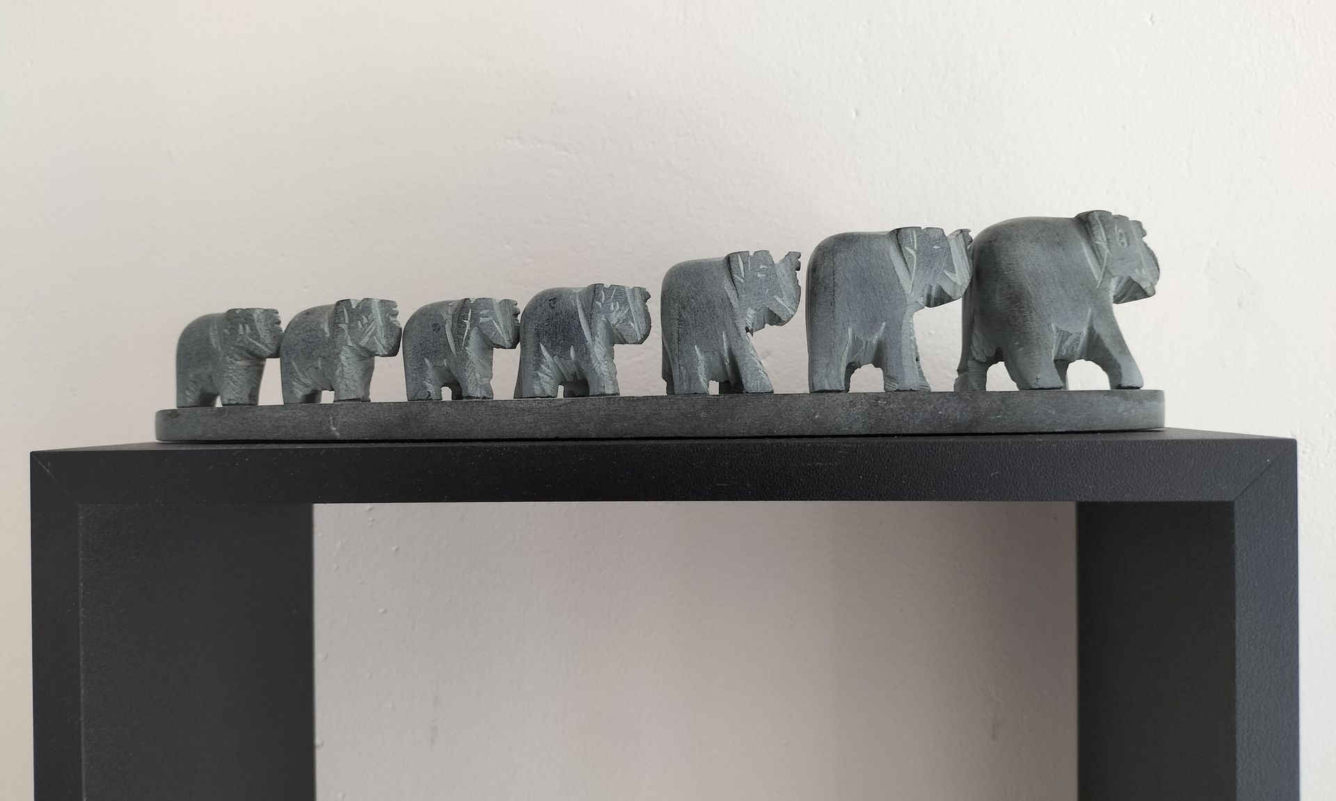 Een stenen sculptuur van een olifantenfamilie staat op een zwarte plank en loopt naar rechts.