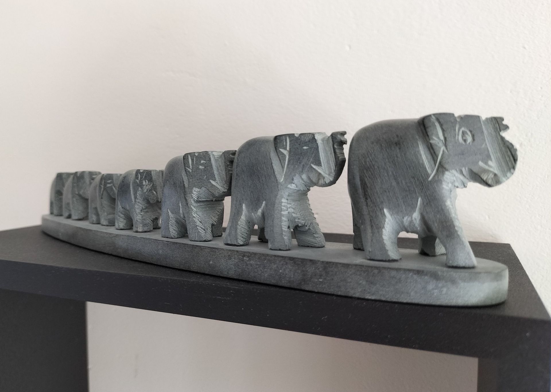 Een stenen sculptuur van een olifantenfamilie staat op een zwarte plank en loopt naar rechts.