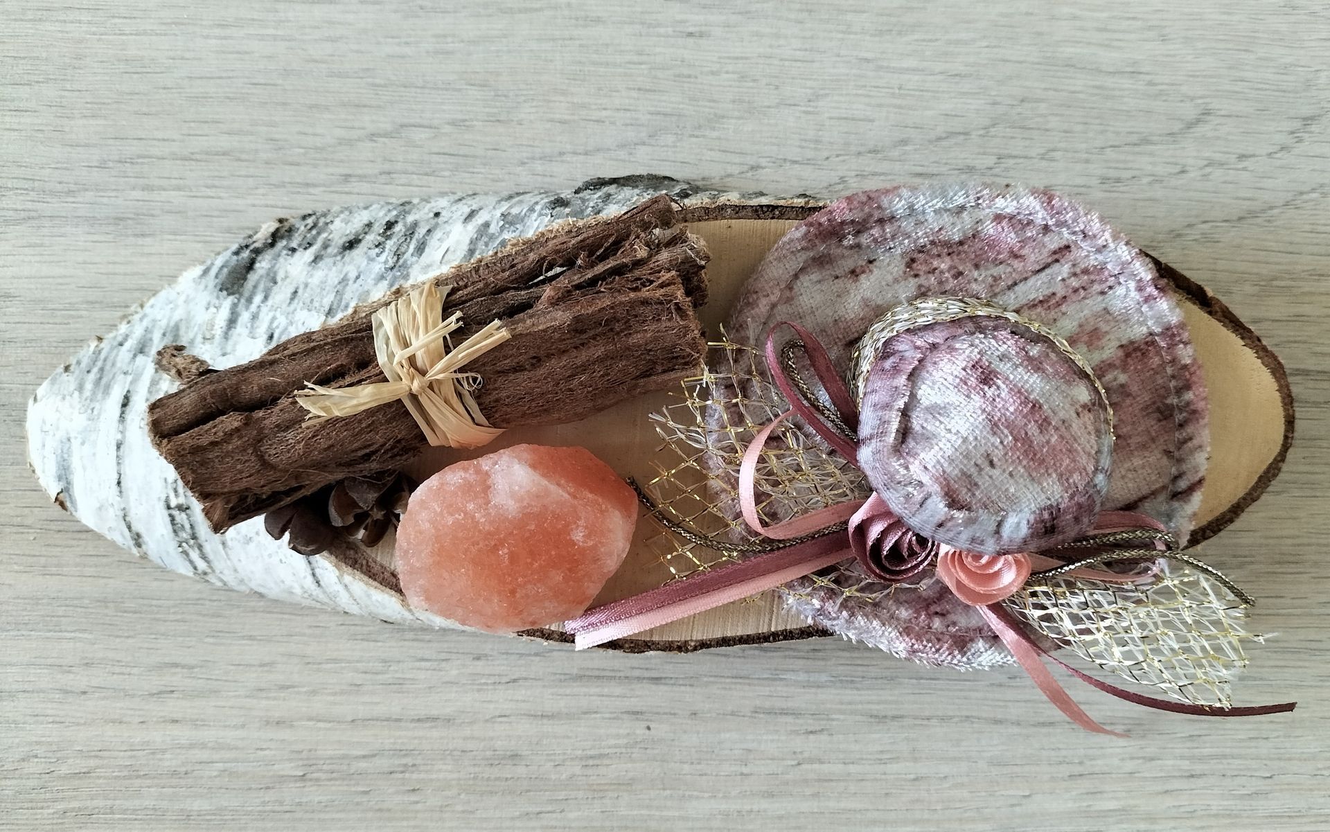 Decoratief arrangement op een berkenhouten schijf: kaneelstokjes, roze accenten en een zoutkristal.