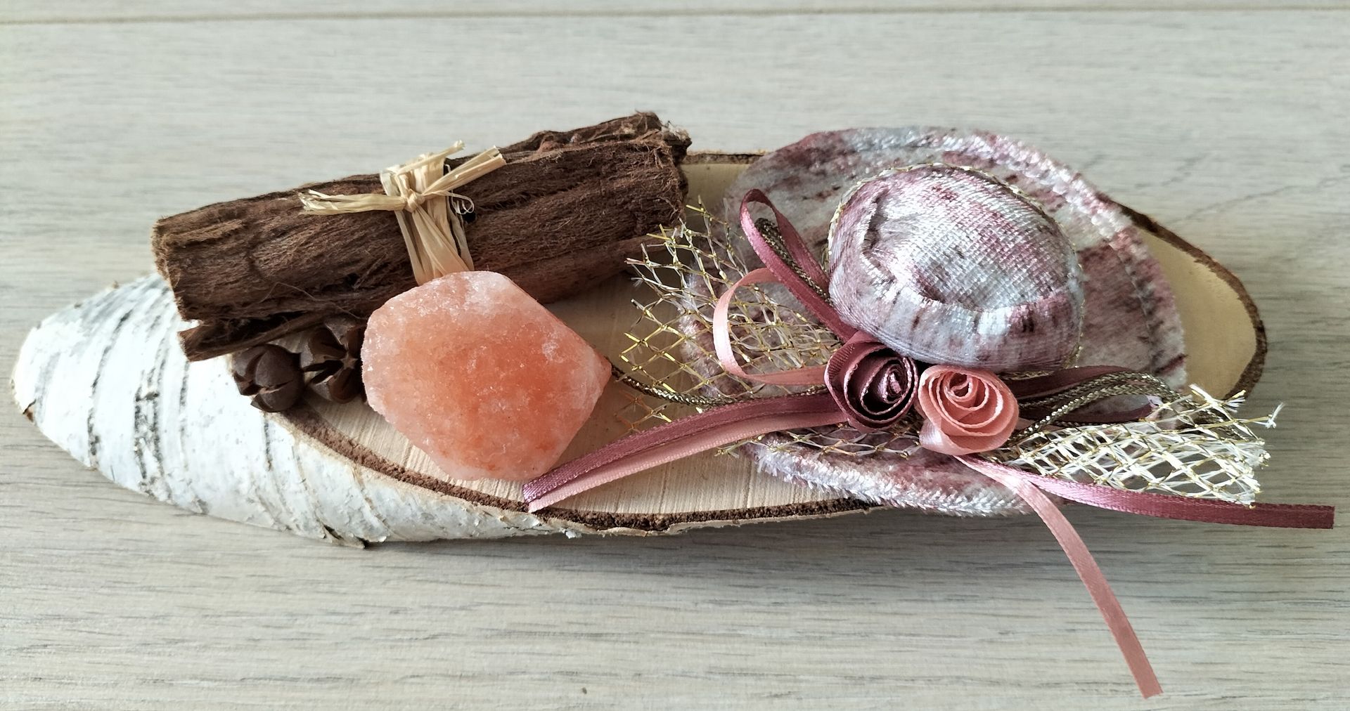 Decoratief arrangement op een berkenhouten schijf: kaneelstokjes, roze accenten en een zoutkristal.