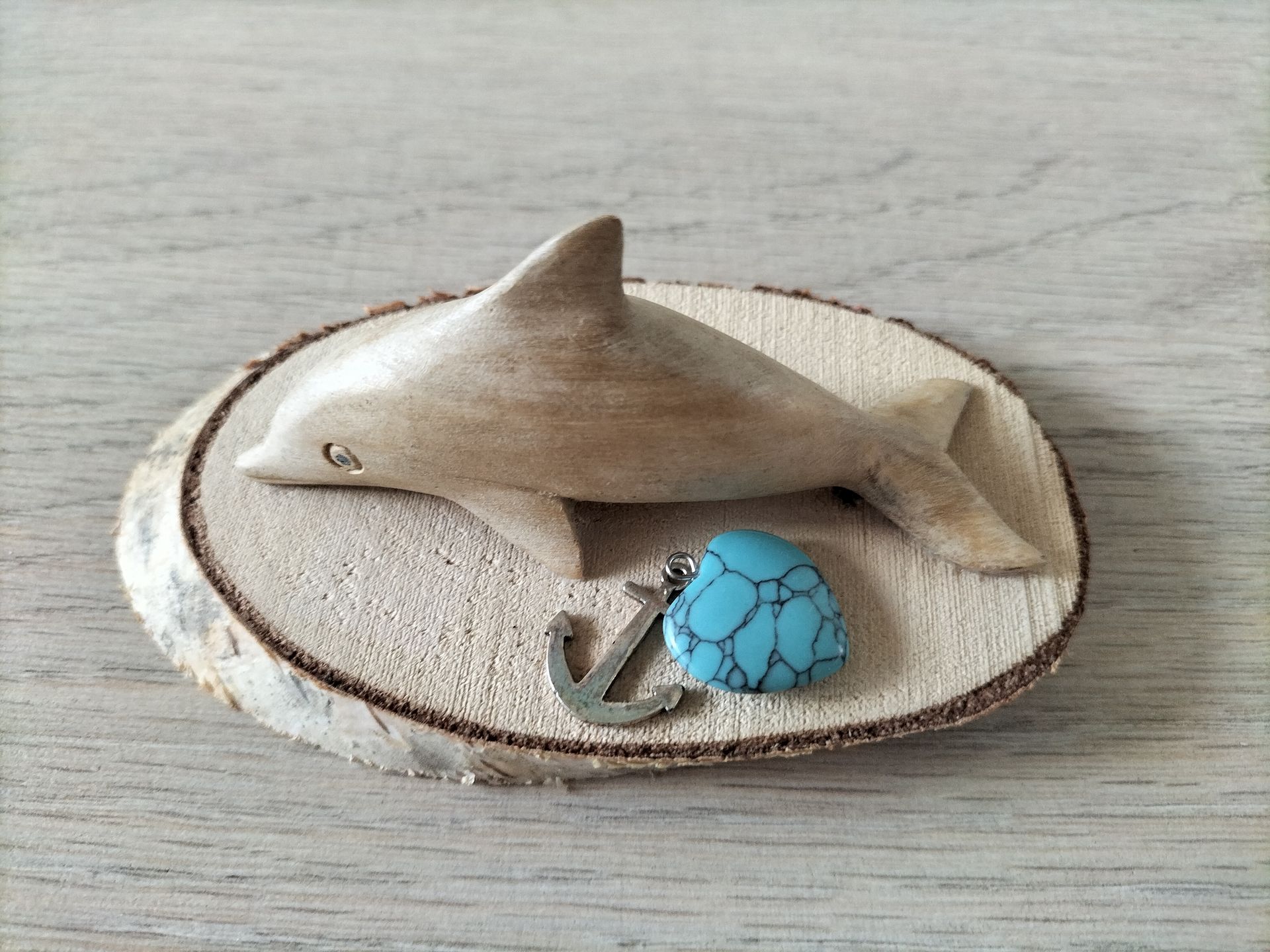 Houten dolfijnsculptuur met turkooizen steen en ankerhanger op een houten schijf.
