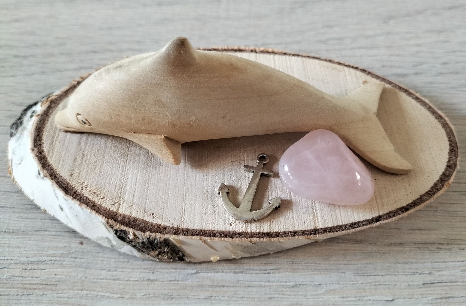 Houten beeldje van een dolfijn op een houten voetstuk met een hartje van rozenkwarts en een metalen anker.