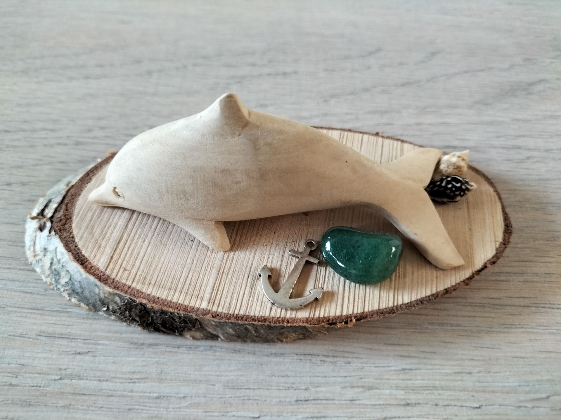 Houten dolfijnsculptuur op een houten schijf met een groene steen en een ankerhanger.