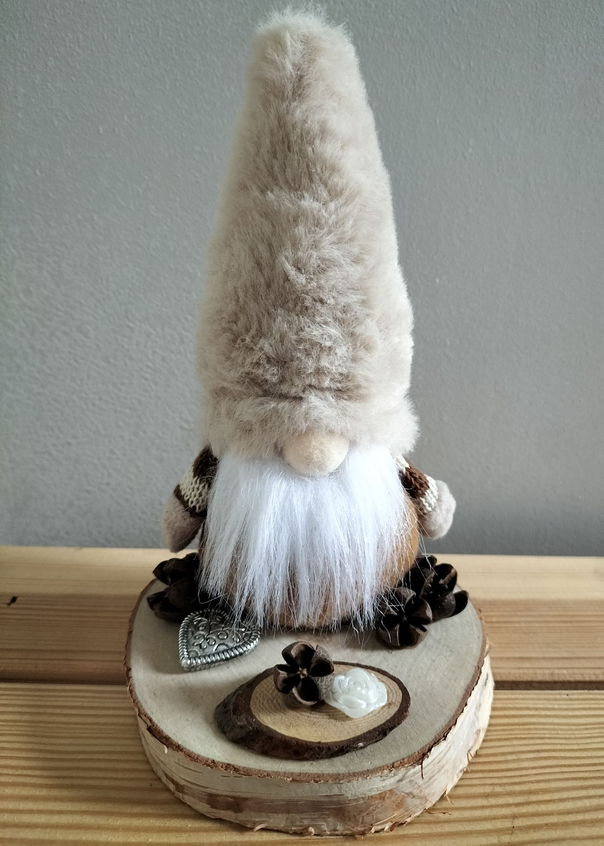 Een kabouterfiguurtje met een lange, lichtbruine hoed en een witte baard, zittend op een houten schijf met dennenappels.