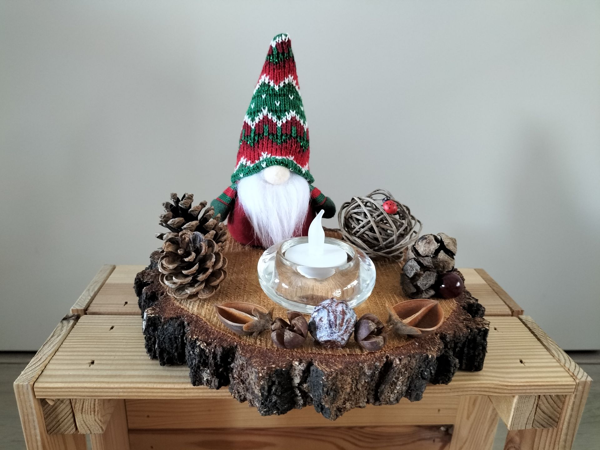 Kerstkabouter als tafeldecoratie op een houten schijf met kaars, dennenappels en decoratieve accenten.
