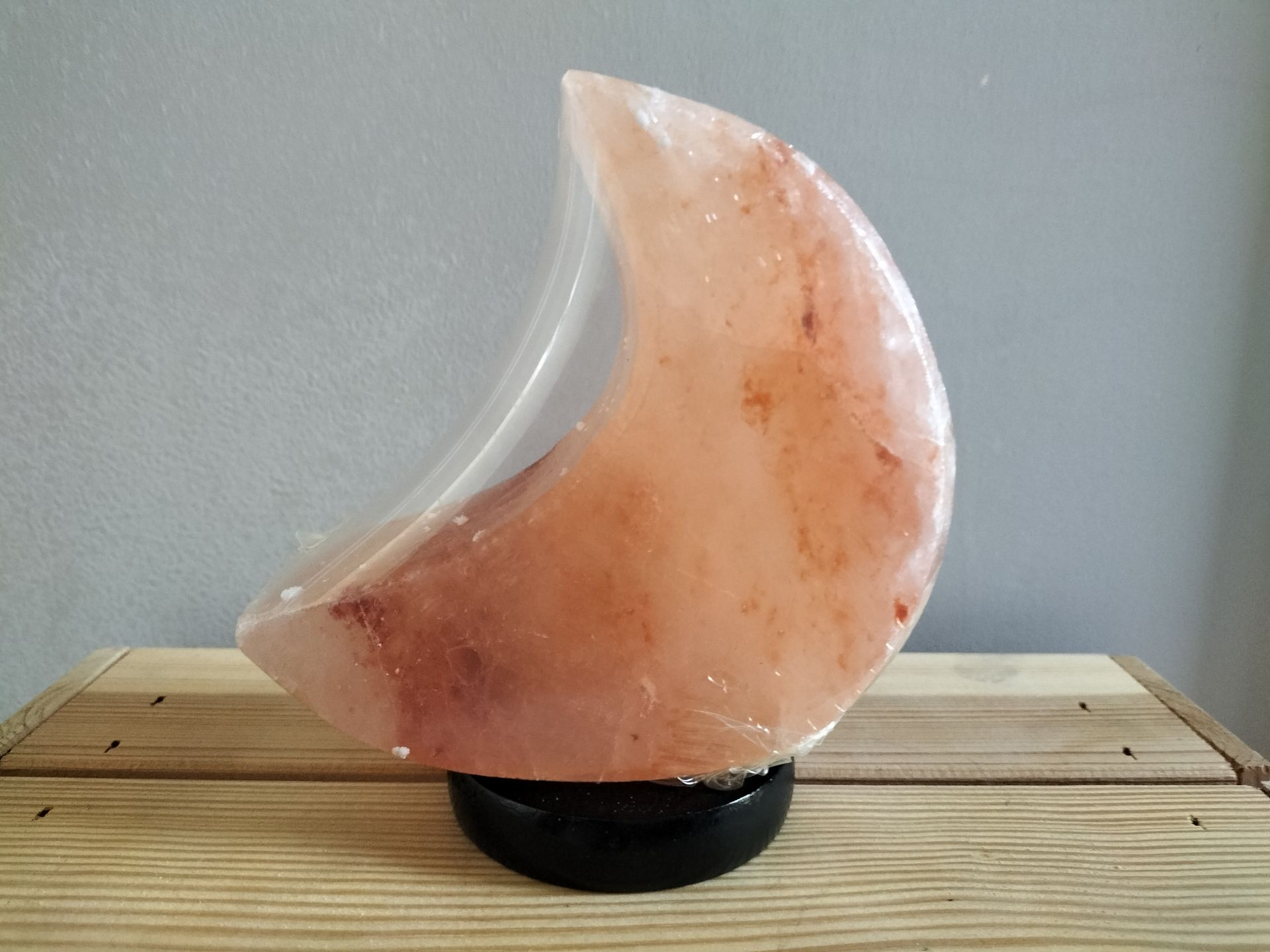 Licht oranje Himalayazoutlamp in de vorm van een halve maan, op een zwarte voet.