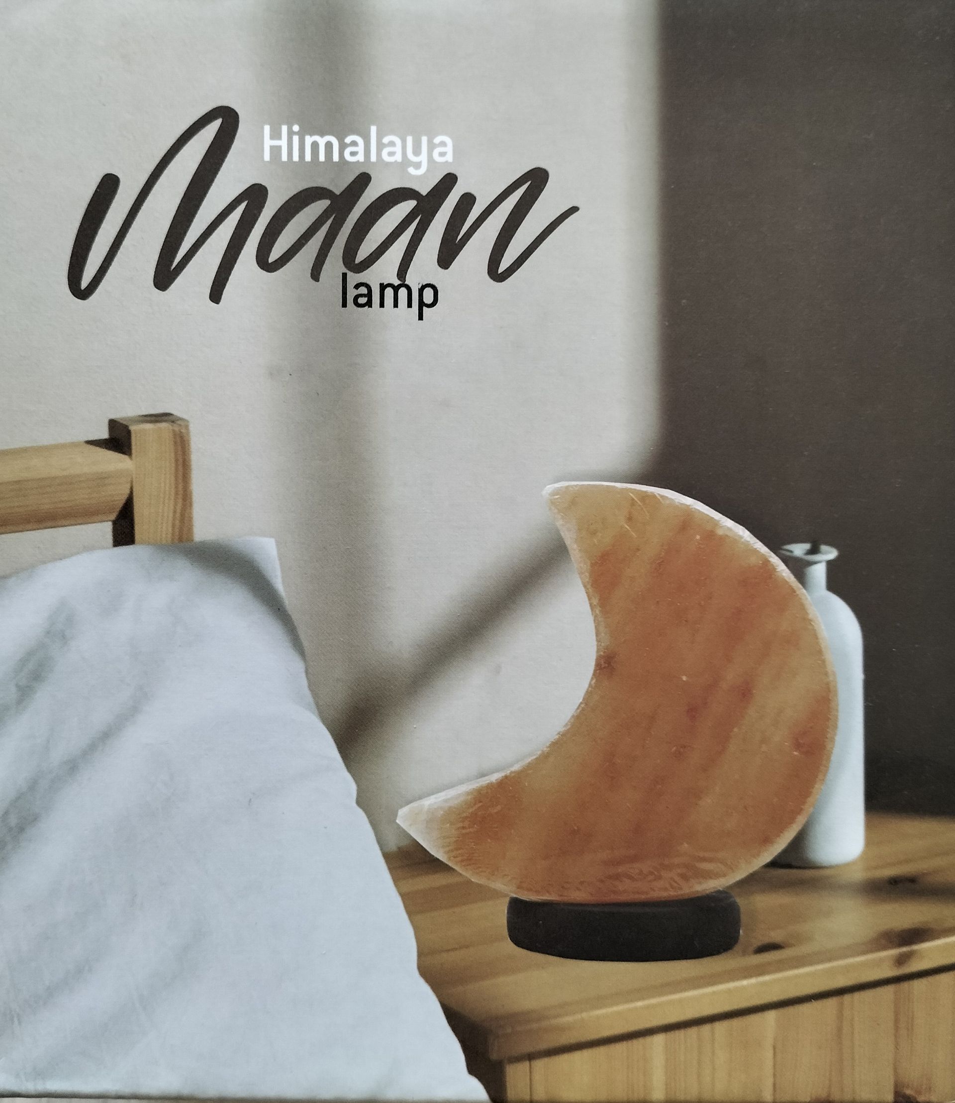 Licht oranje Himalayazoutlamp in de vorm van een halve maan, op een zwarte voet.