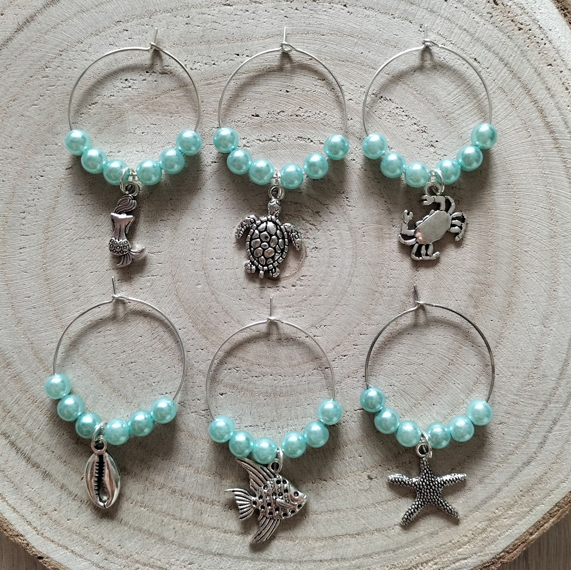 Zes wijnhangertjes van kralen, elk met een hanger in de vorm van een zeedier, in blauw en zilver.