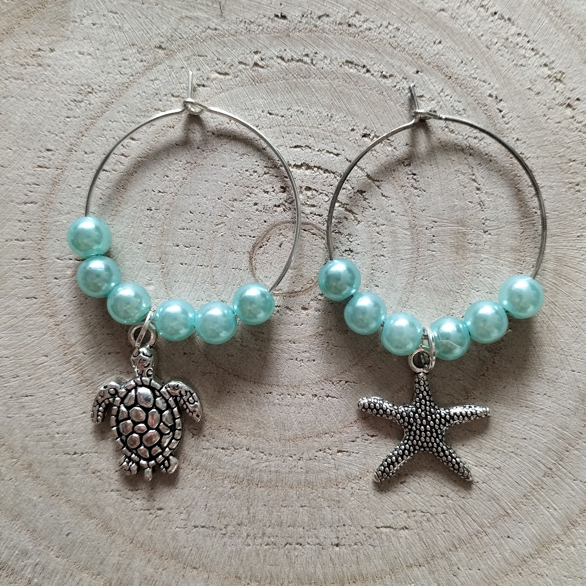 Zes wijnhangertjes van kralen, elk met een hanger in de vorm van een zeedier, in blauw en zilver.