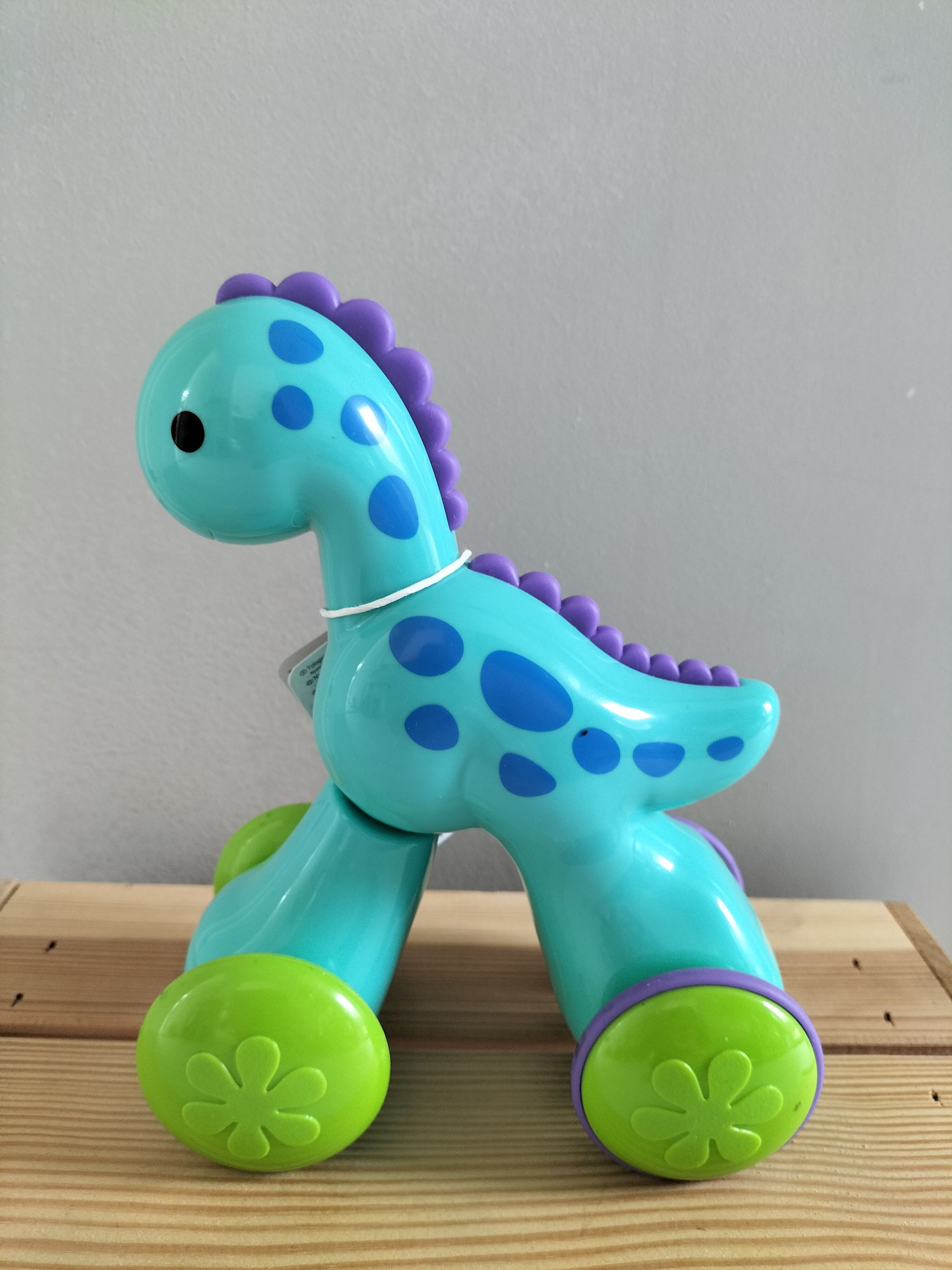 Push & Go Racer Dino. Een turquoise en paarse dinosaurus met groene wielen.
