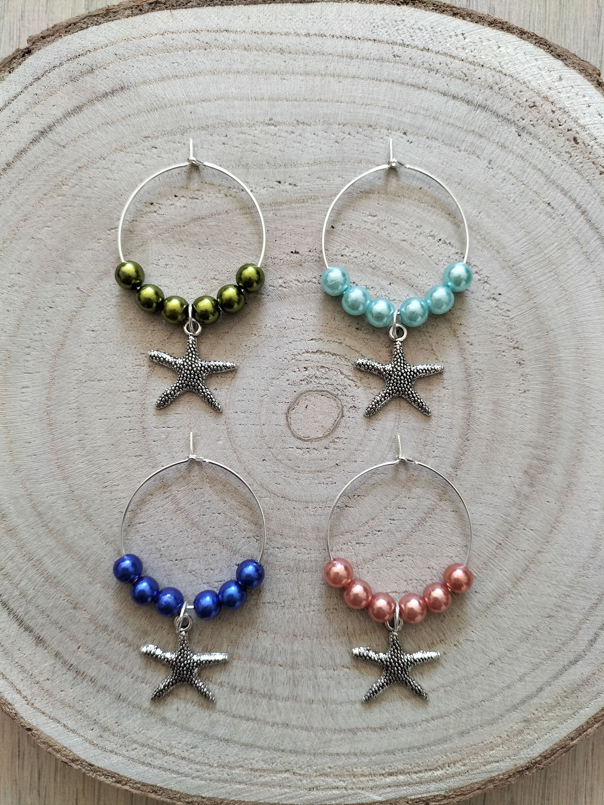 Vier wijnringetjes met kralen en hangers in de vorm van een zeester. Olijfgroene, blauwe, turquoise en koraalkleurige kralen.