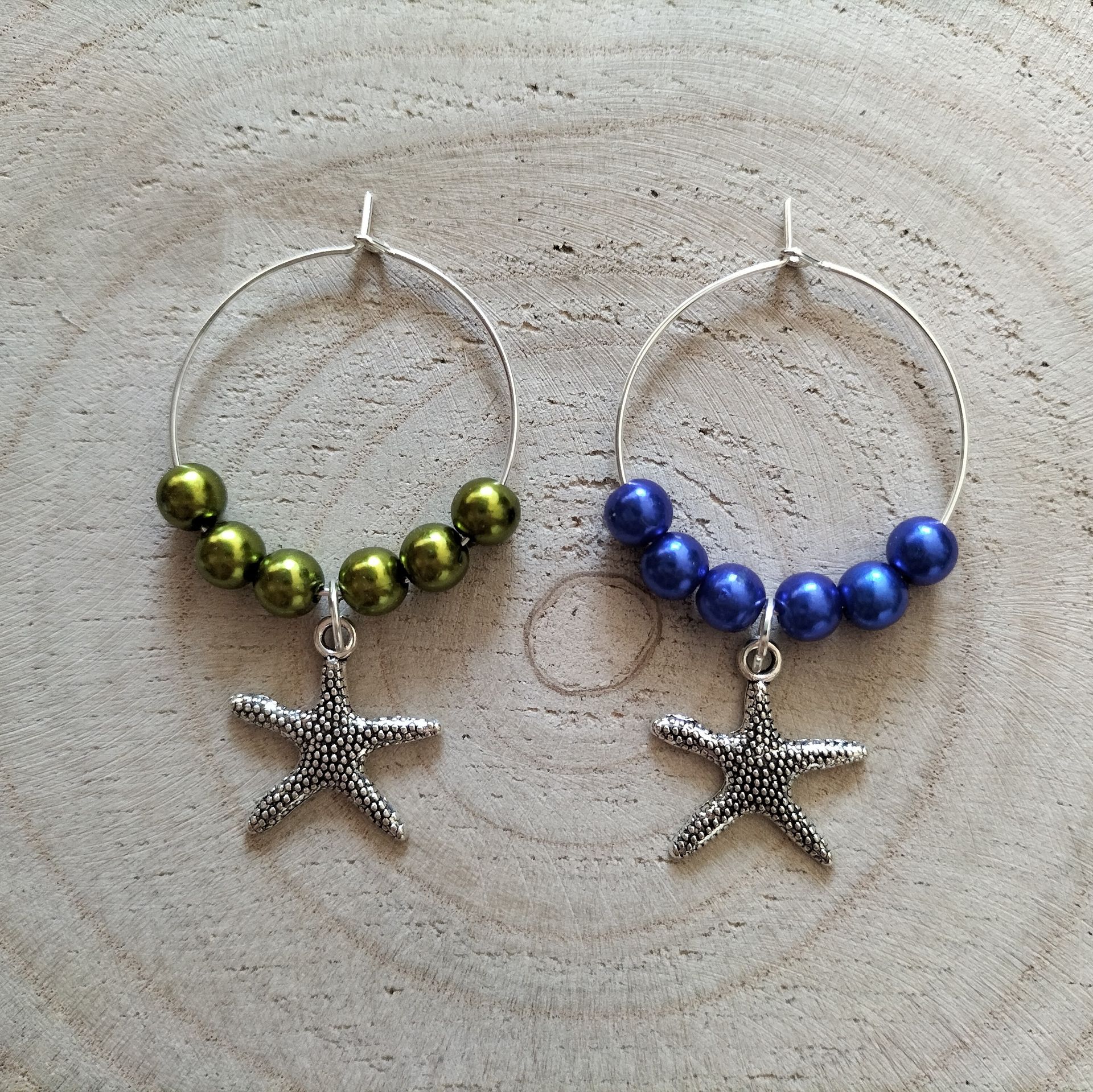 Vier wijnringetjes met kralen en hangers in de vorm van een zeester. Olijfgroene, blauwe, turquoise en koraalkleurige kralen.