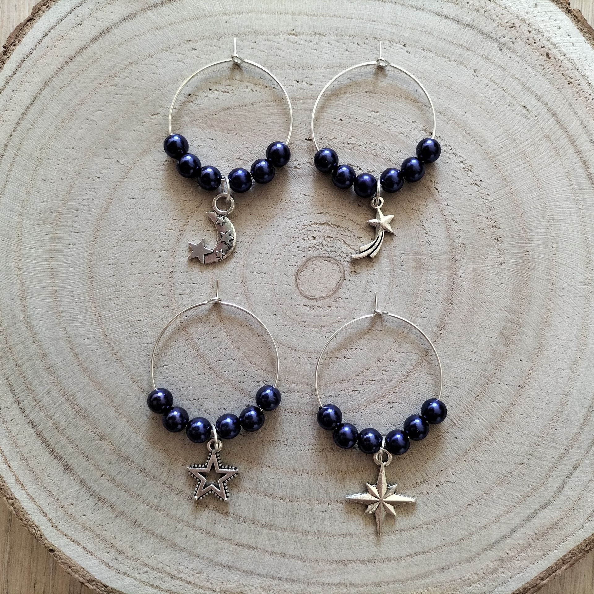 Vier zilveren oorringen met donkerblauwe kralen en hemelse bedeltjes op een houten ondergrond.
