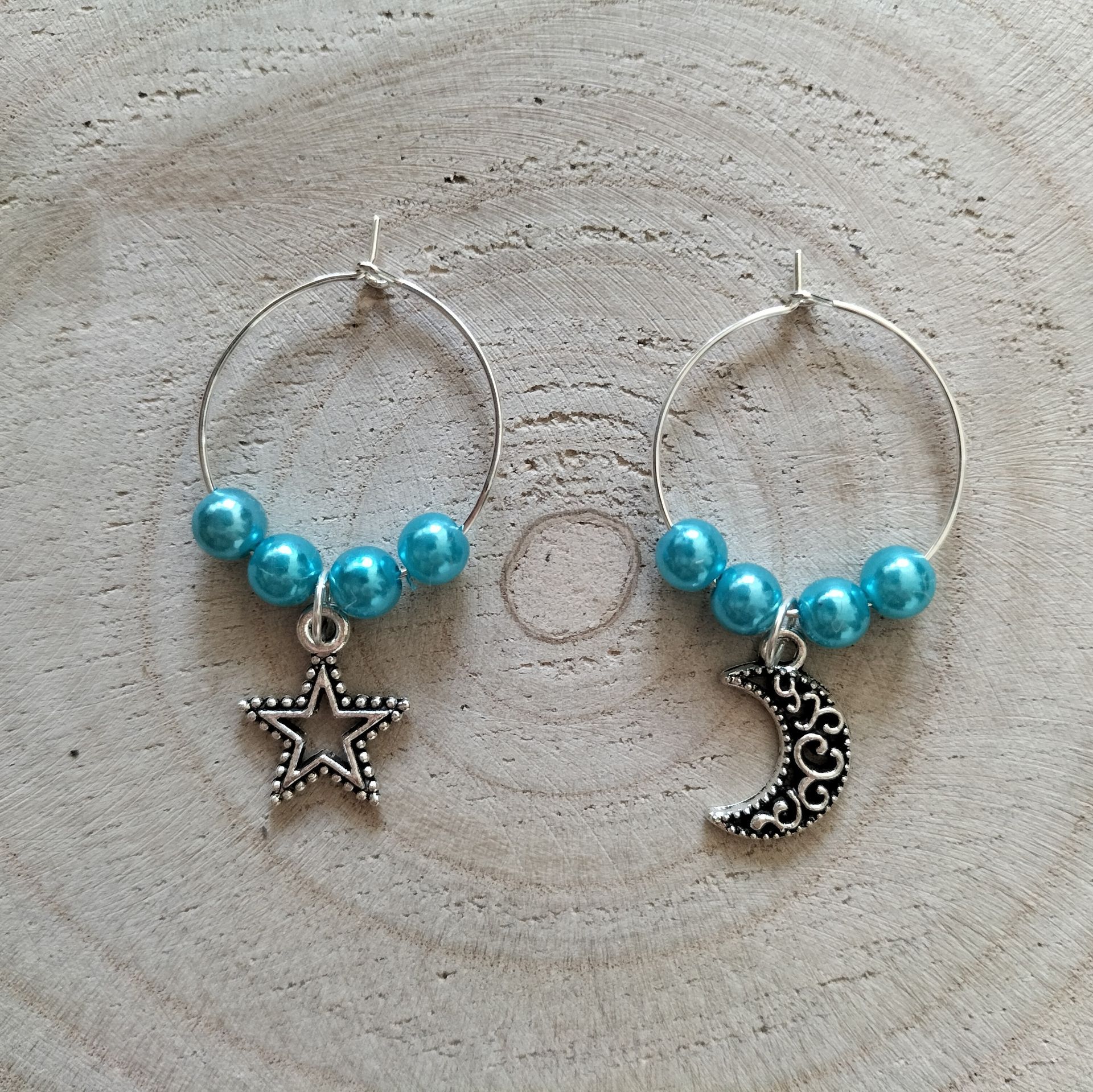 Een paar oorringen: de ene met een sterretje, de andere met een maantje, beide met blauwe kraaltjes.