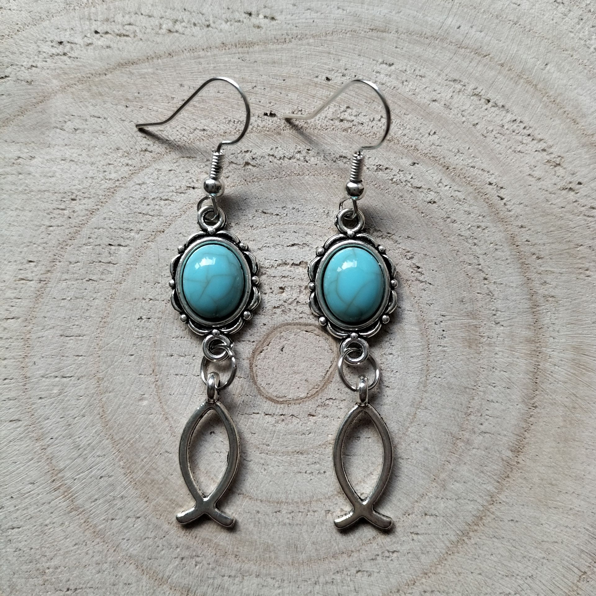 Zilverkleurige oorbellen met ovaalvormig turquoise steentje en ichthus visje, hypoallergeen.
