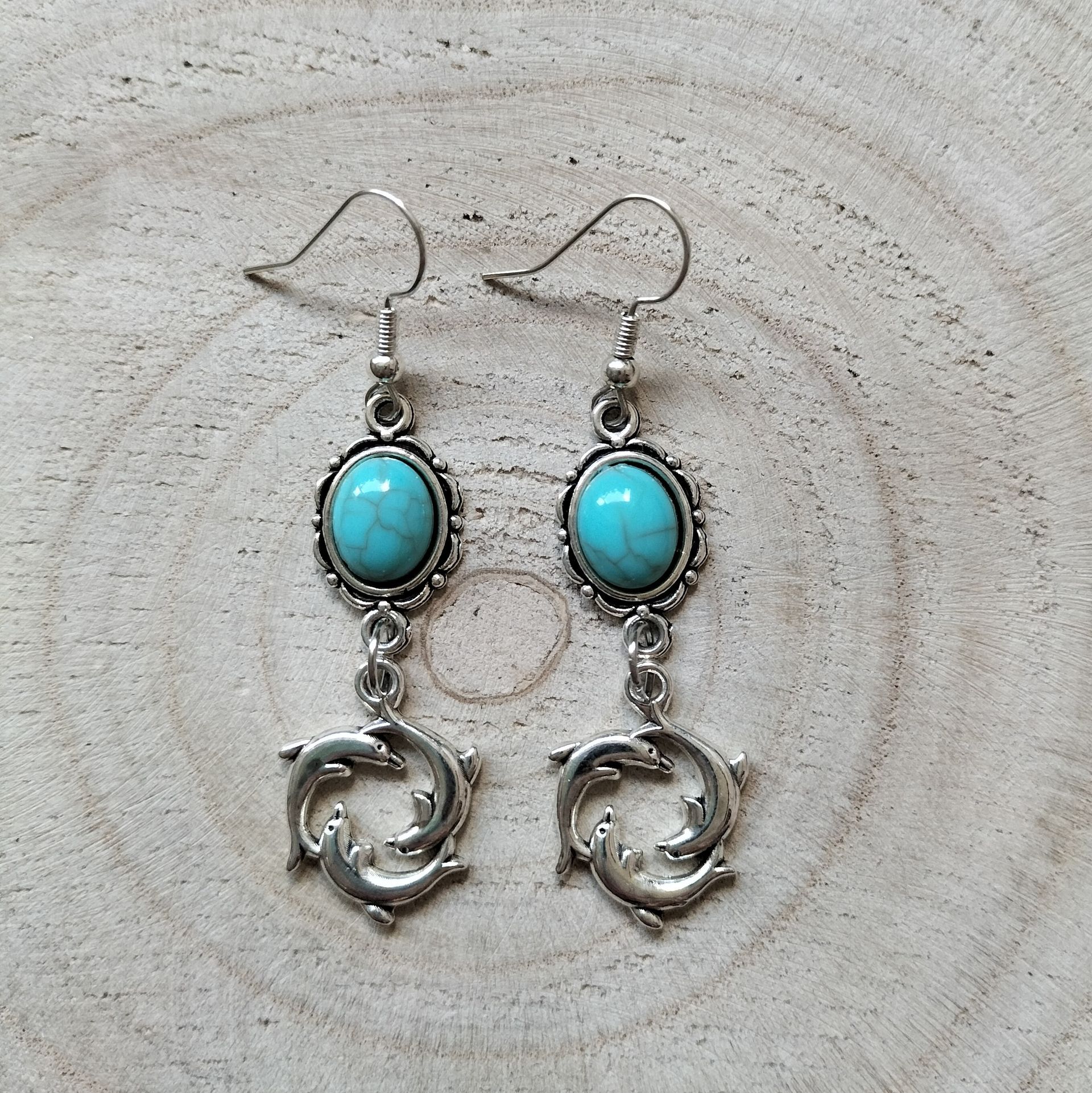 Zilverkleurige oorbellen met ovaalvormig turquoise steentje en dolfijnen, hypoallergeen.