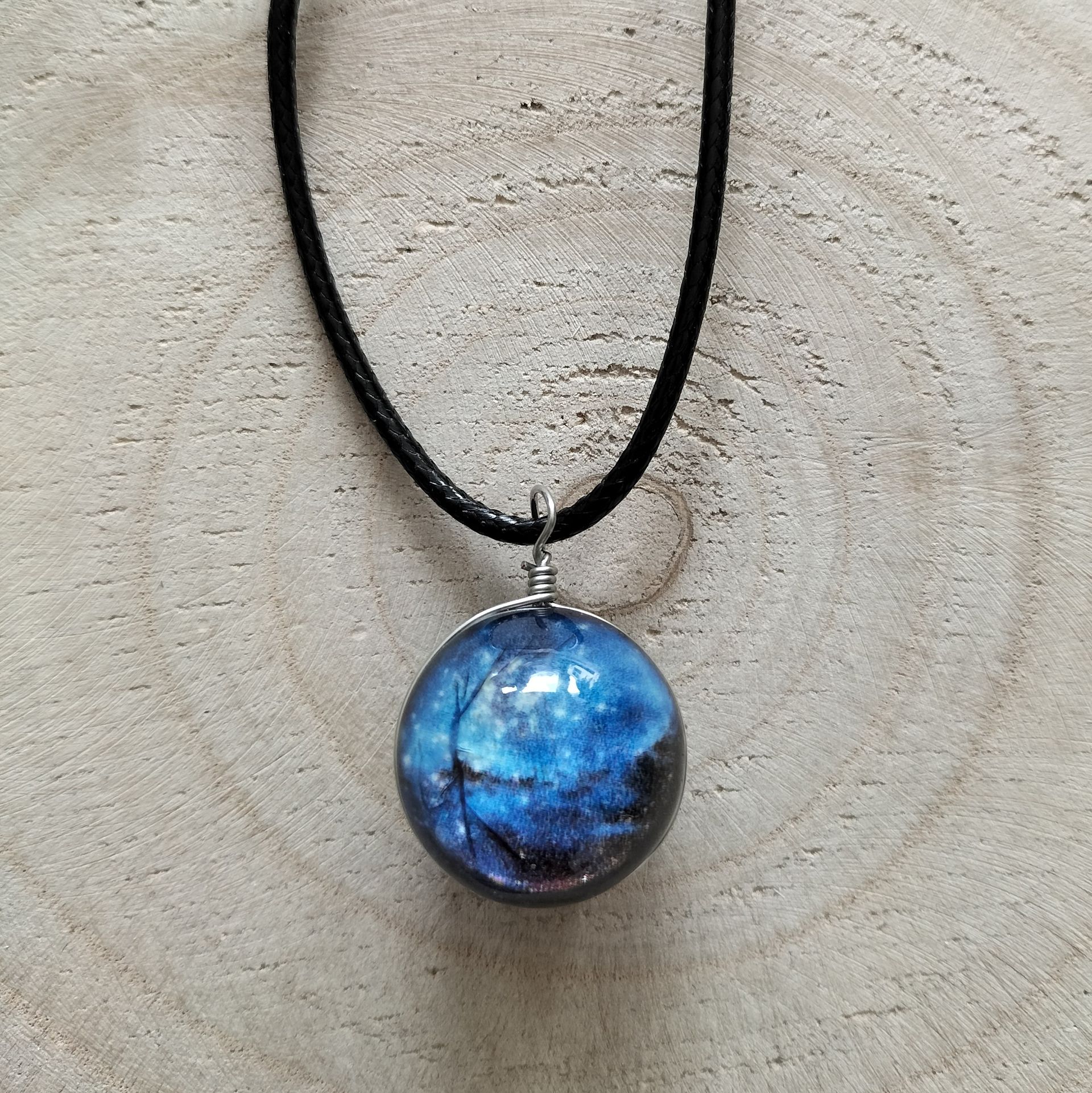 Ketting met een blauw-zwarte bolvormige hanger, gewikkeld op een zwart koord, op een houten achtergrond.