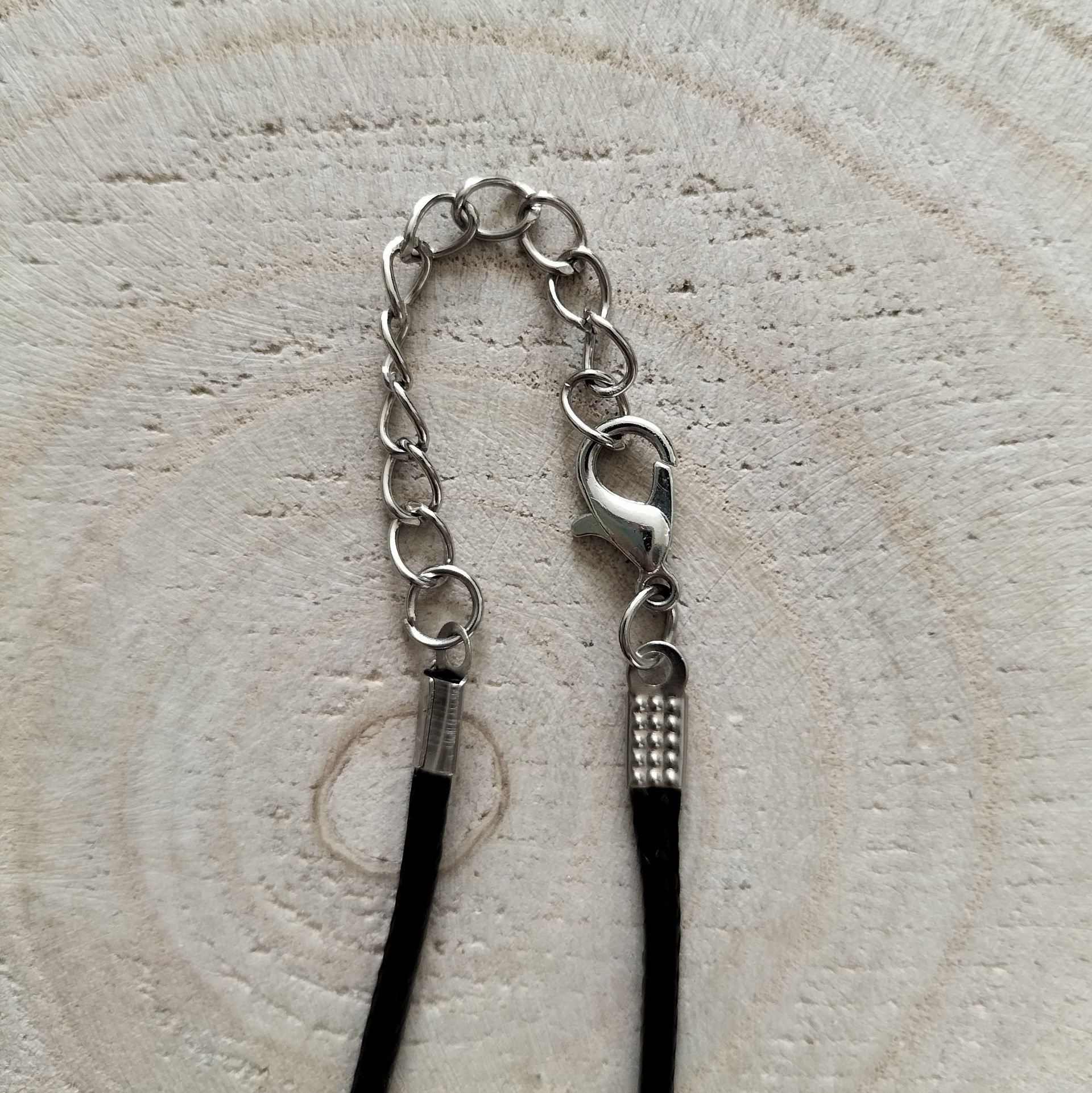 Ketting met een blauw-zwarte bolvormige hanger, gewikkeld op een zwart koord, op een houten achtergrond.