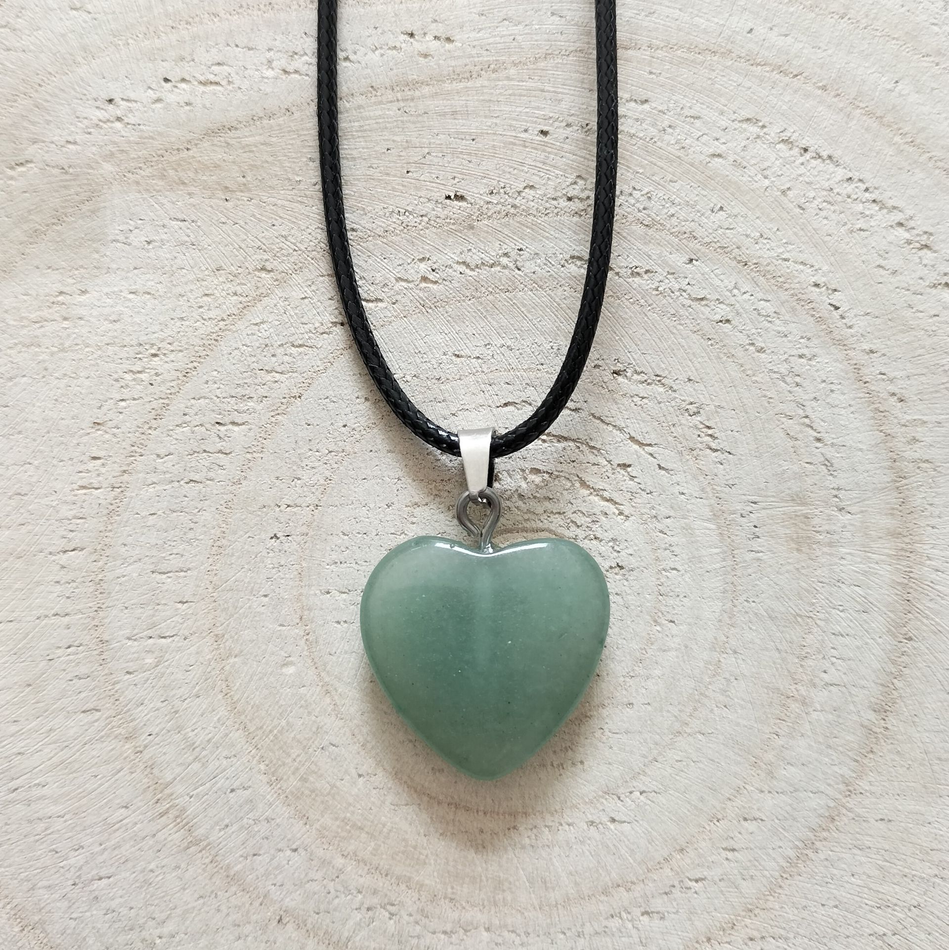 Groene hartvormige stenen hanger aan een zwart koord, geplaatst tegen een achtergrond met houtnerf.