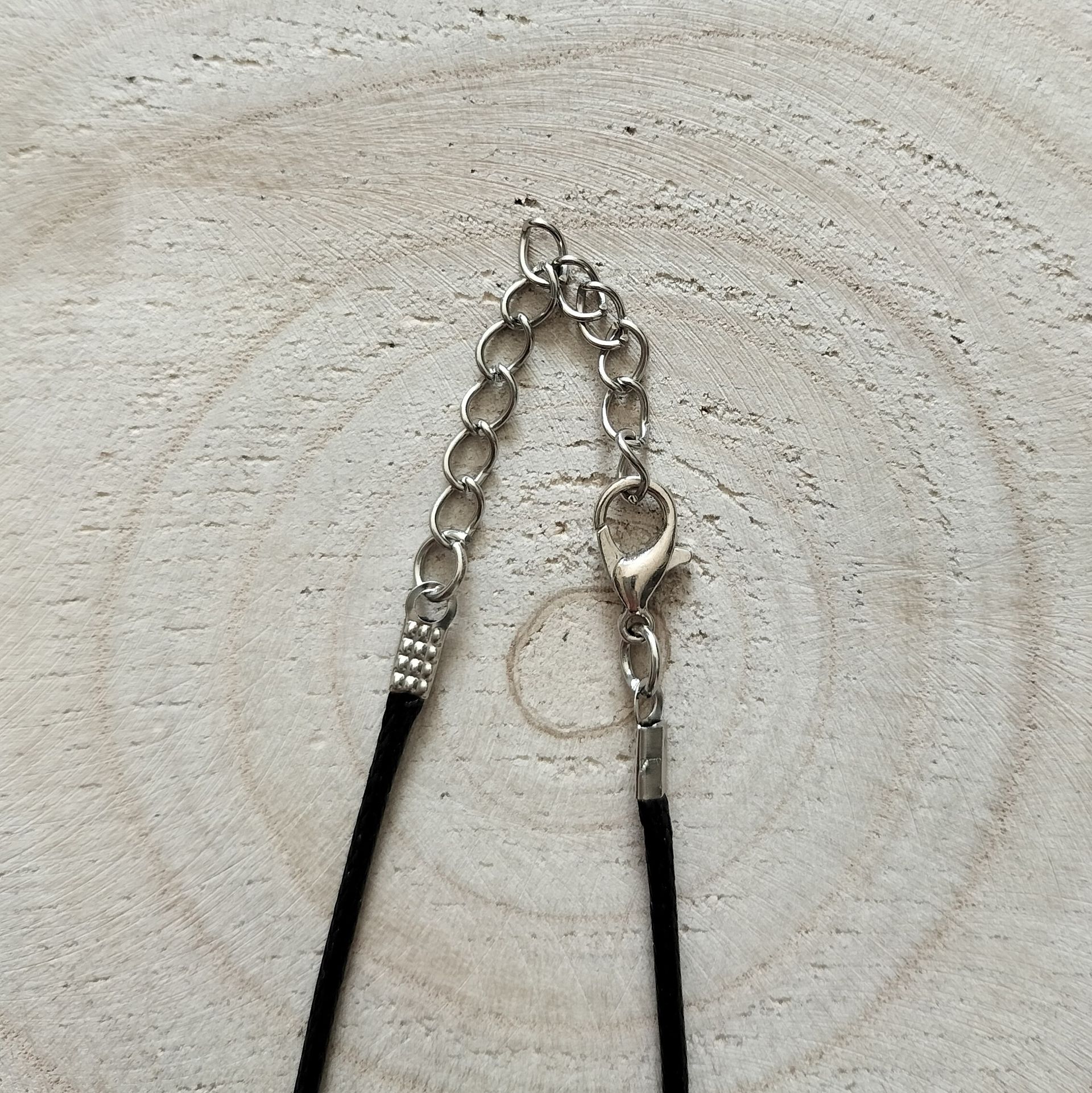Een ketting met een turquoise hartvormige hanger aan een zwart koord, met een achtergrond van houtnerf.