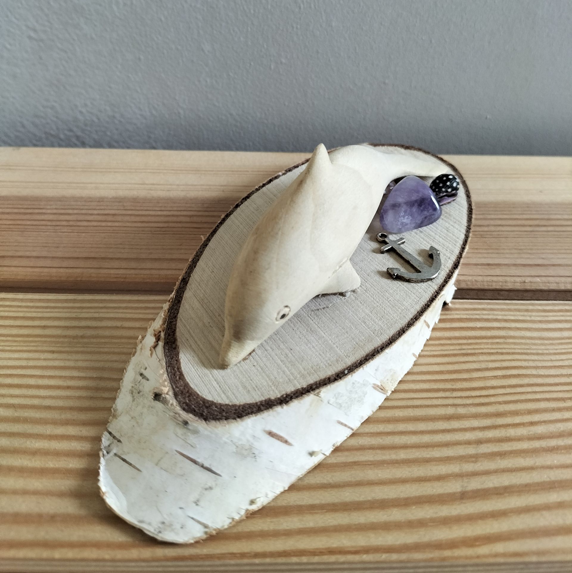 Houten dolfijnsculptuur op een berkenhouten schijf, met anker, dobbelstenen en steen; op een houten ondergrond.