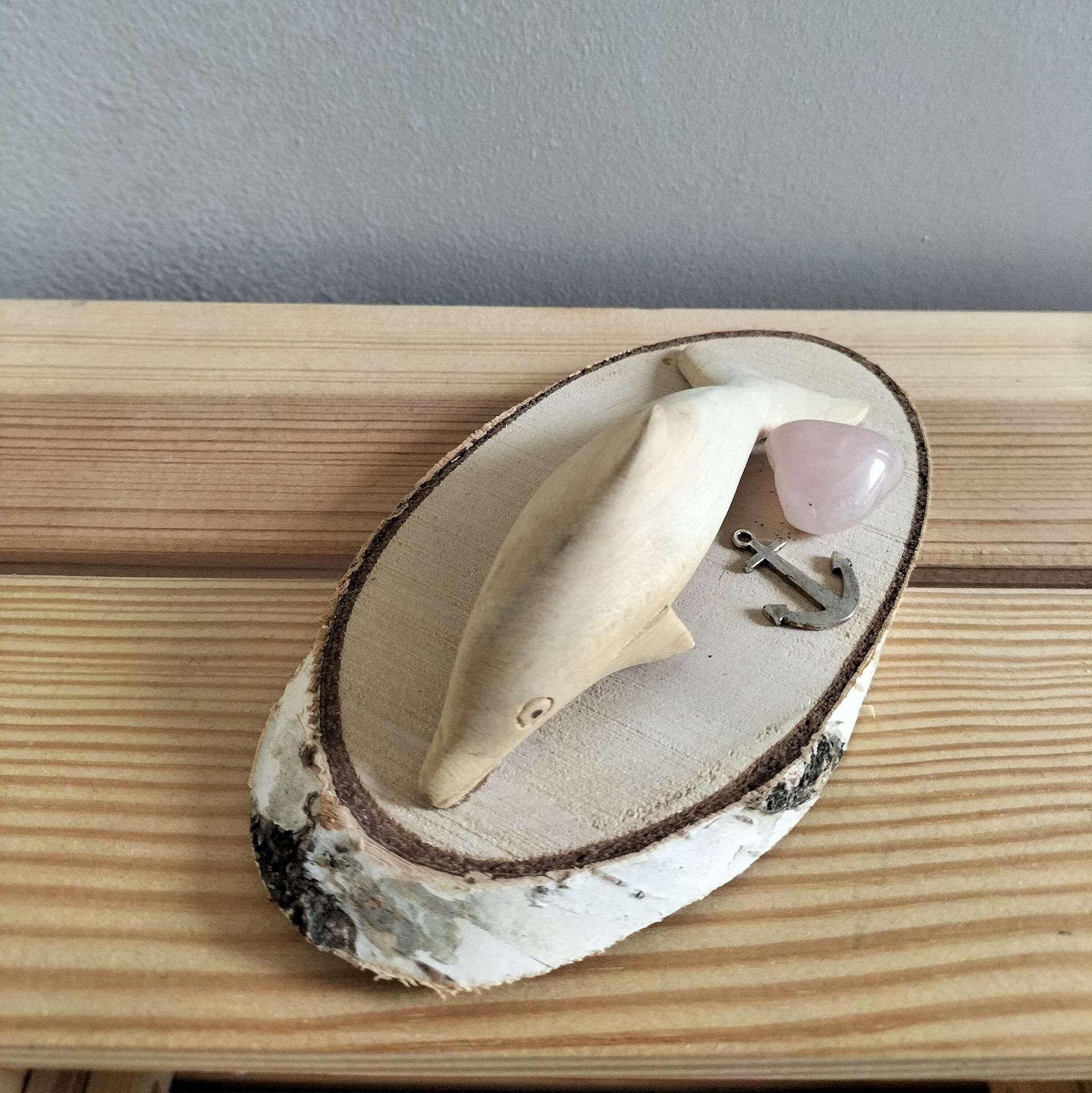 Houten beeldje van een dolfijn op een houten voetstuk met een hartje van rozenkwarts en een metalen anker.