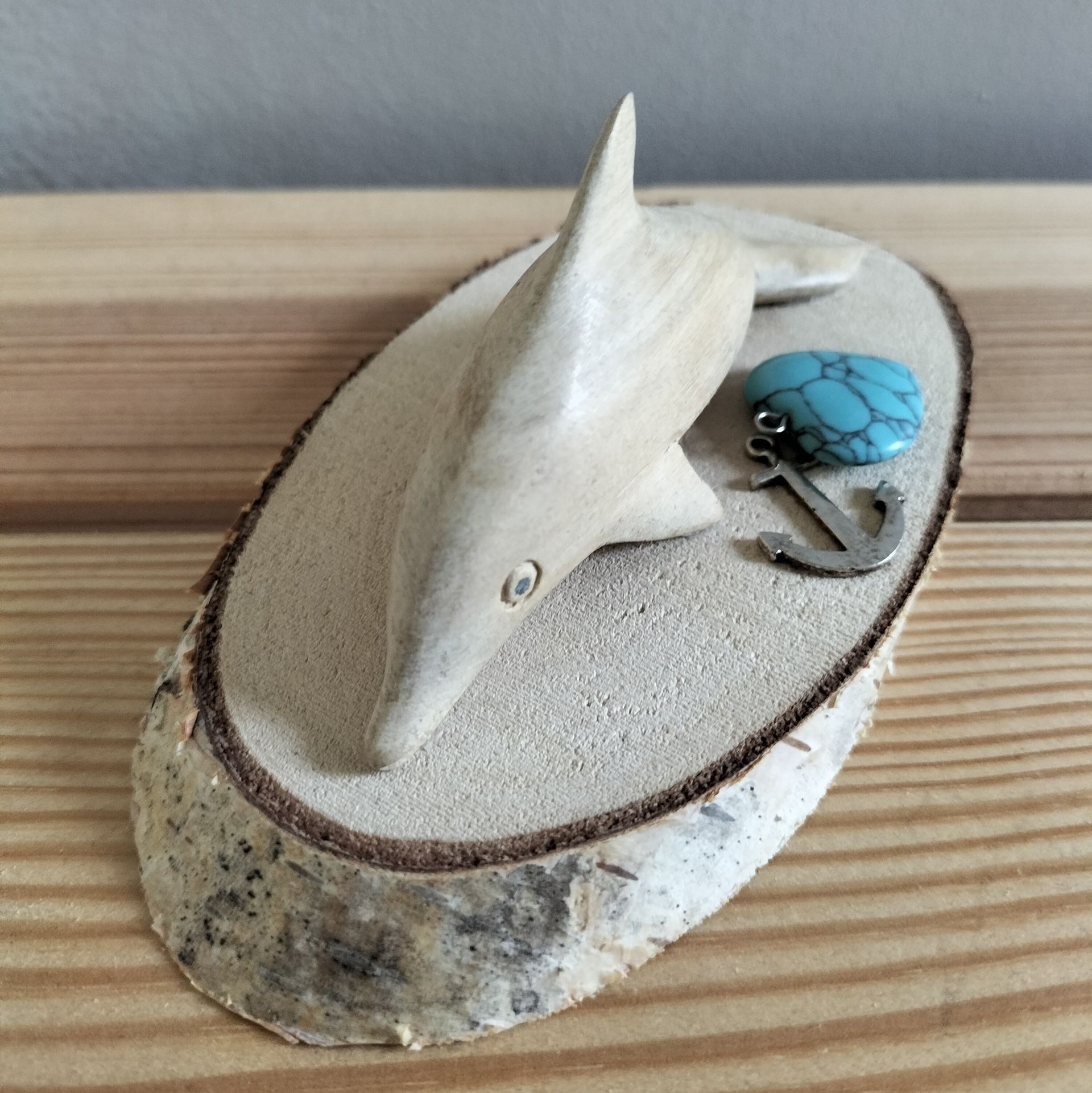 Houten dolfijnsculptuur met turkooizen steen en ankerhanger op een houten schijf.