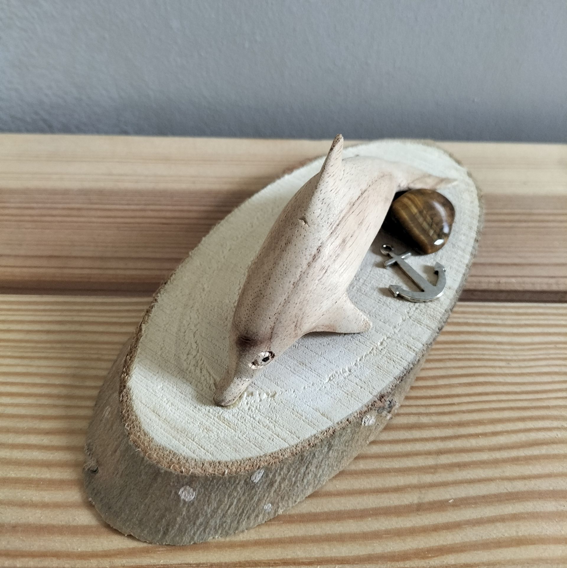 Een houten dolfijnsculptuur op een houten schijf als sokkel, met een tijgeroogsteen en een klein anker.