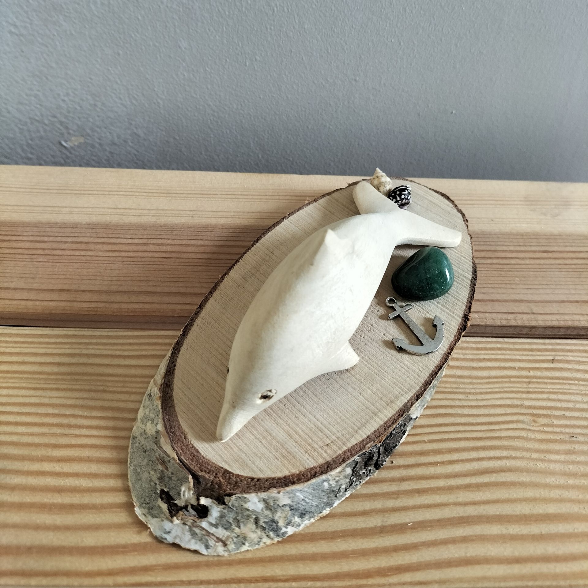 Houten dolfijnsculptuur op een houten schijf met een groene steen en een ankerhanger.