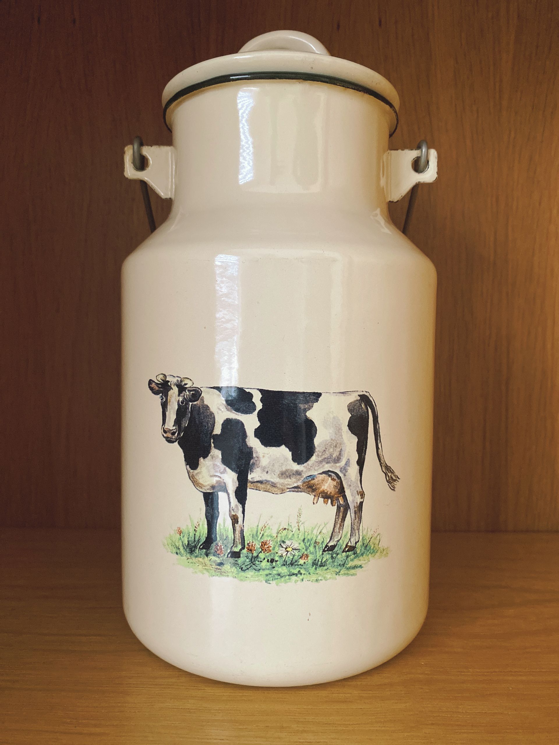 Vintage geëmailleerde melkbus met een koeienafbeelding.