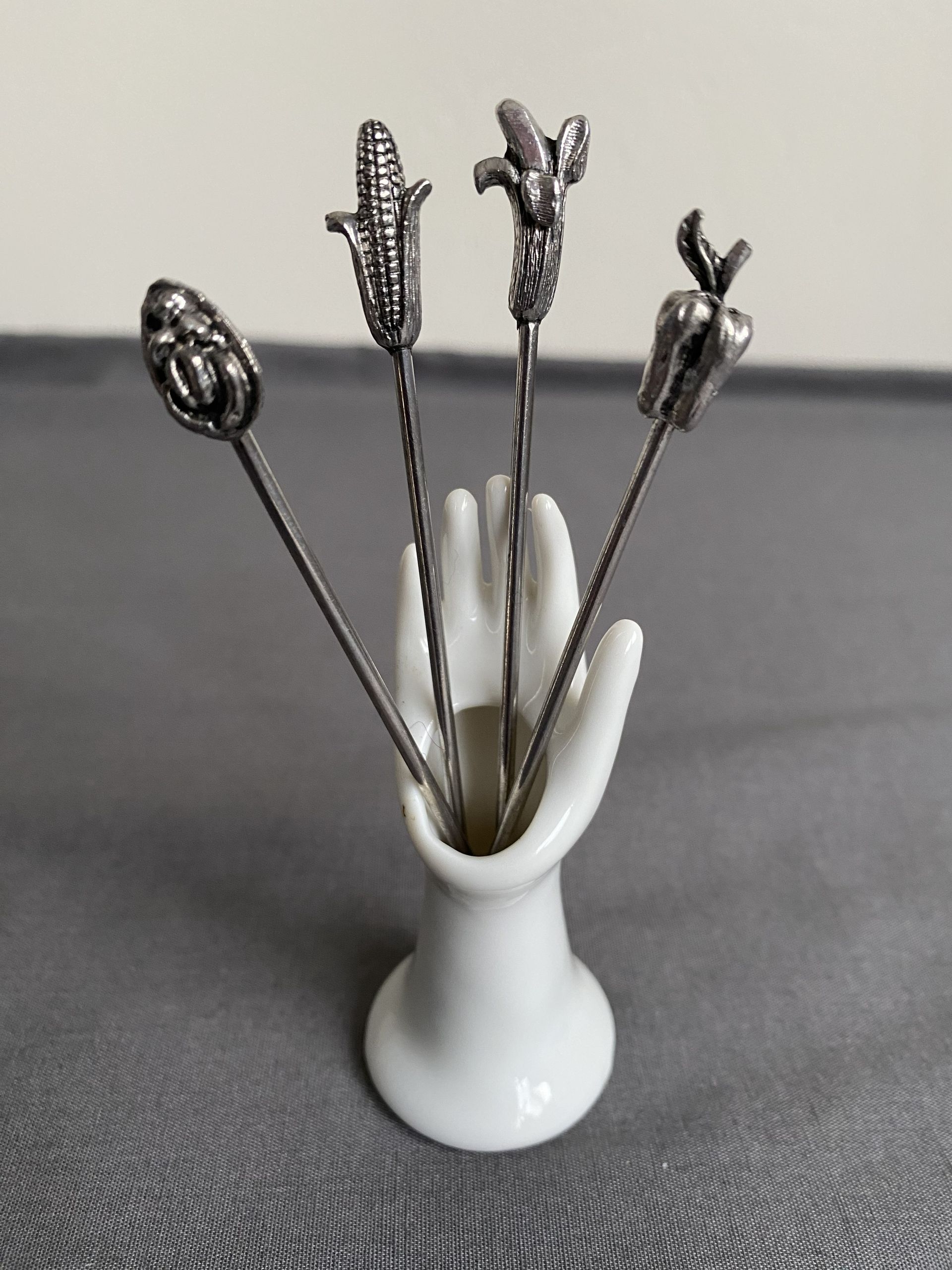 Vintage witte keramieken houder in de vorm van een hand met 4 verzilverde cocktailvorkjes.