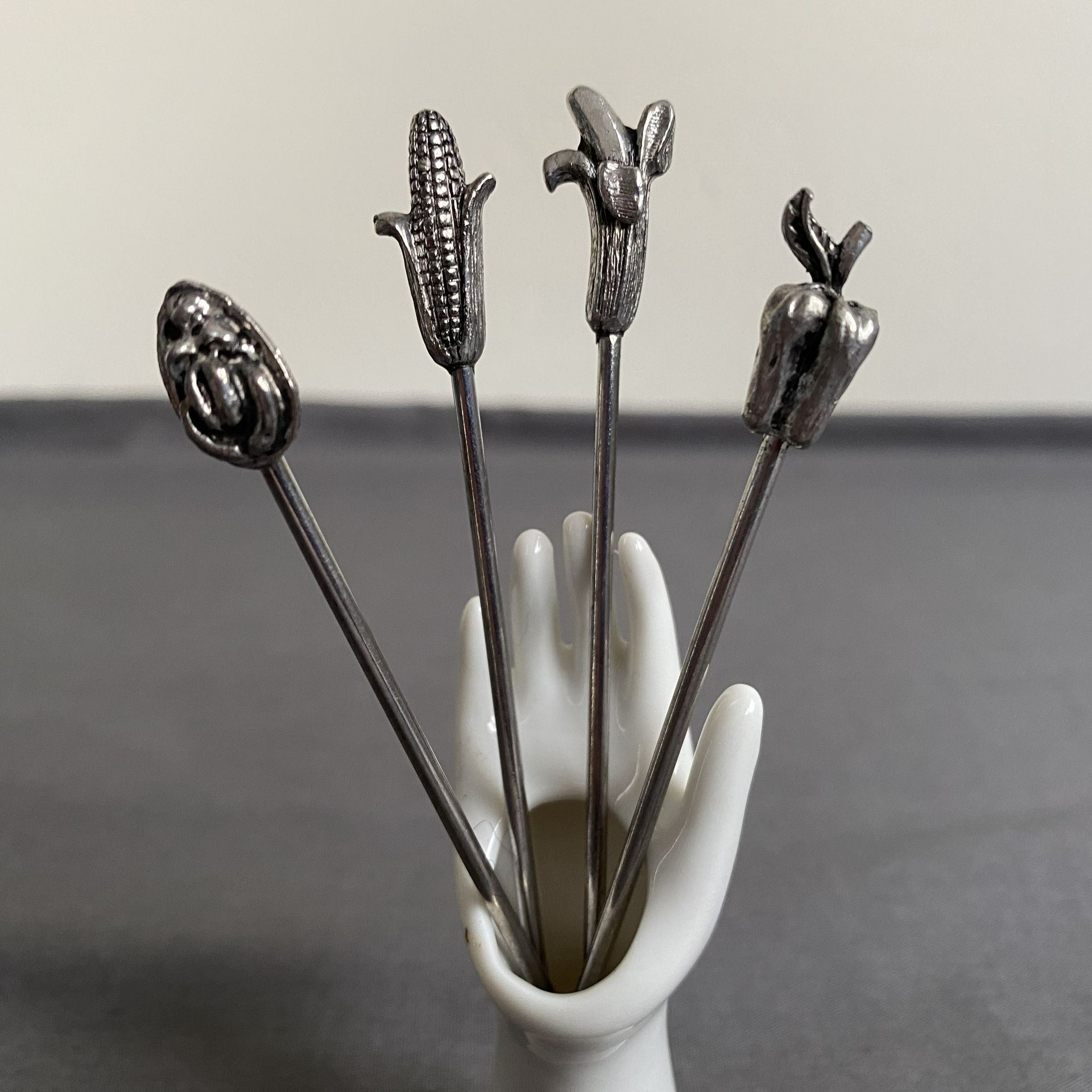 Vintage witte keramieken houder in de vorm van een hand met 4 verzilverde cocktailvorkjes.