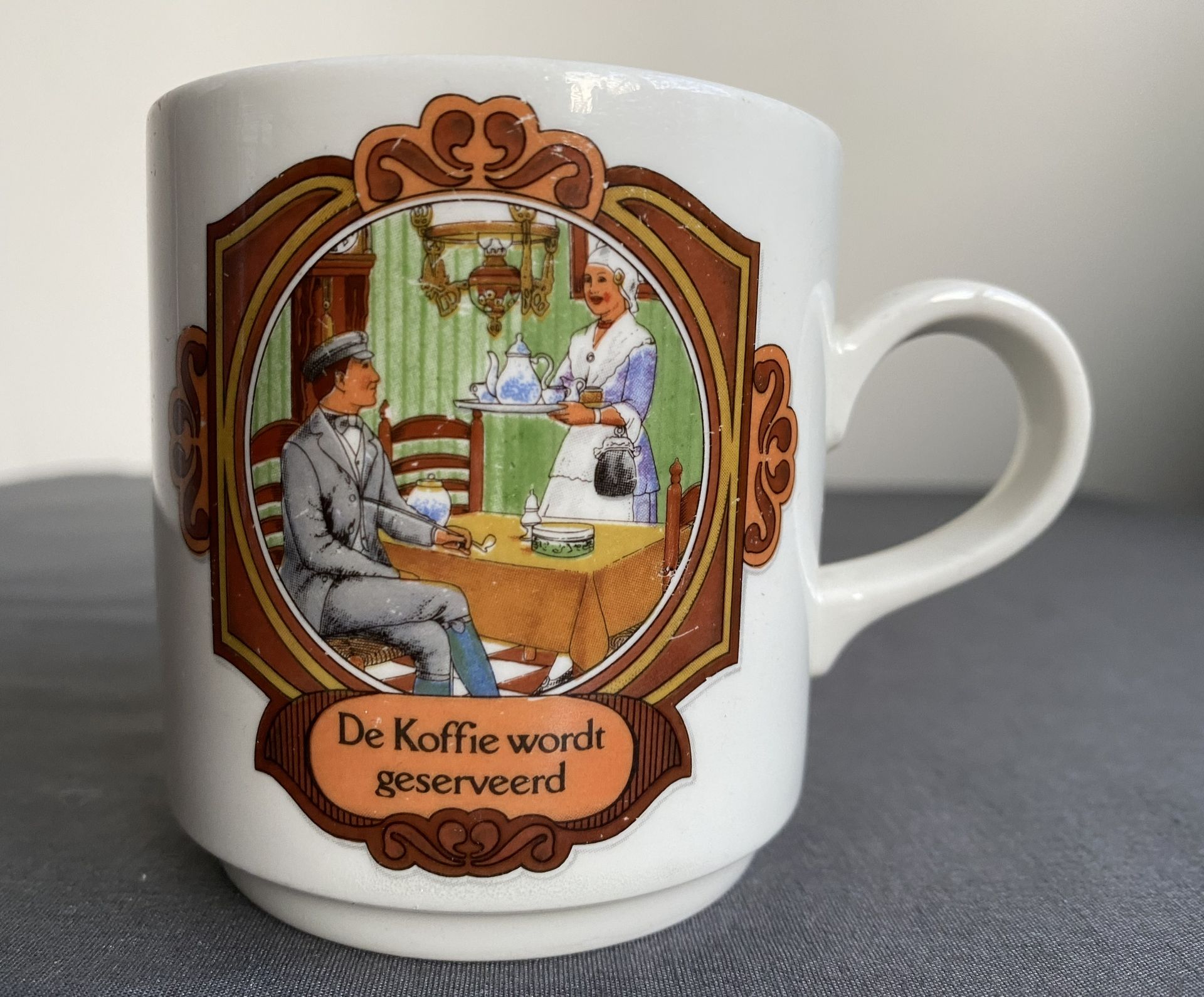 Koffiemok met afbeelding van een ober die koffie brengt naar een man die aan een tafel zit. Tekst: 