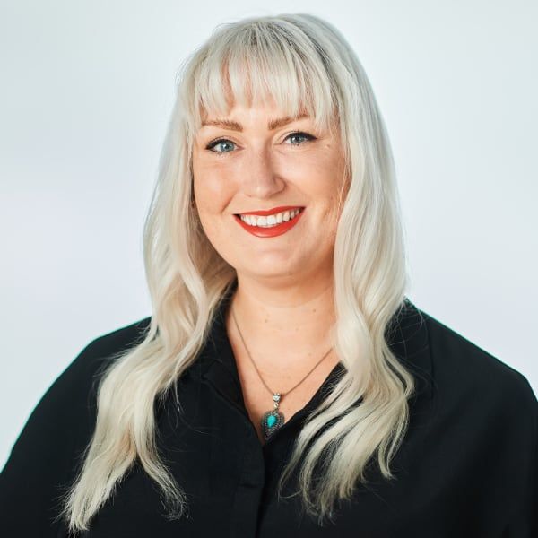 A woman with blonde hair is wearing a black shirt and a necklace.