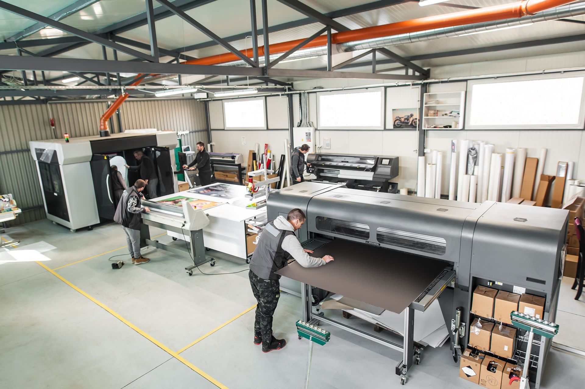 A man is standing in front of a large printer in a factory