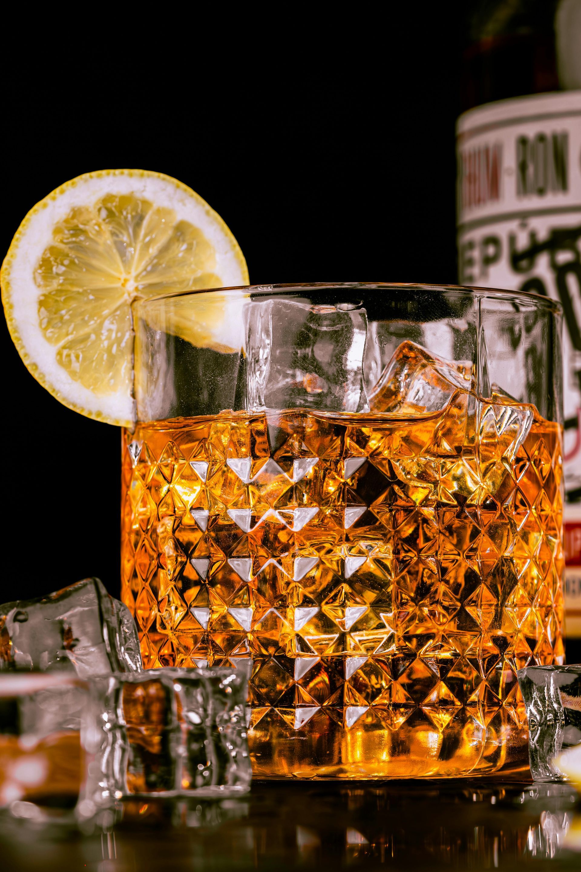 Cocktail in textured glass with lemon slice and ice, dark background.