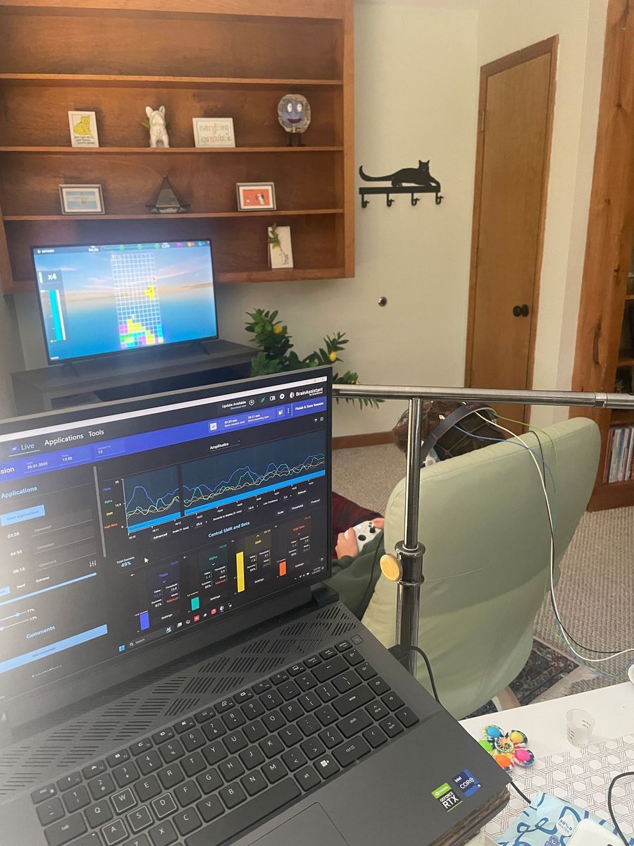 Laptop displaying data in front of a desk. A second laptop and bookcase are visible. A chair and some items are nearby.