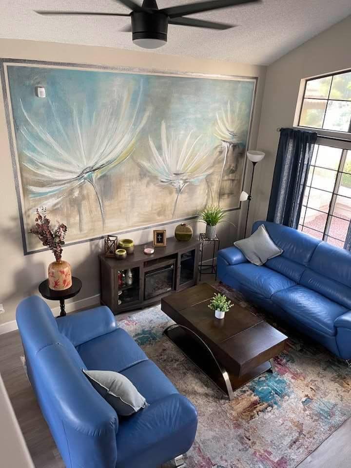 A modern living room with two blue sofas, a wooden coffee table, and a large abstract floral wall art piece.
