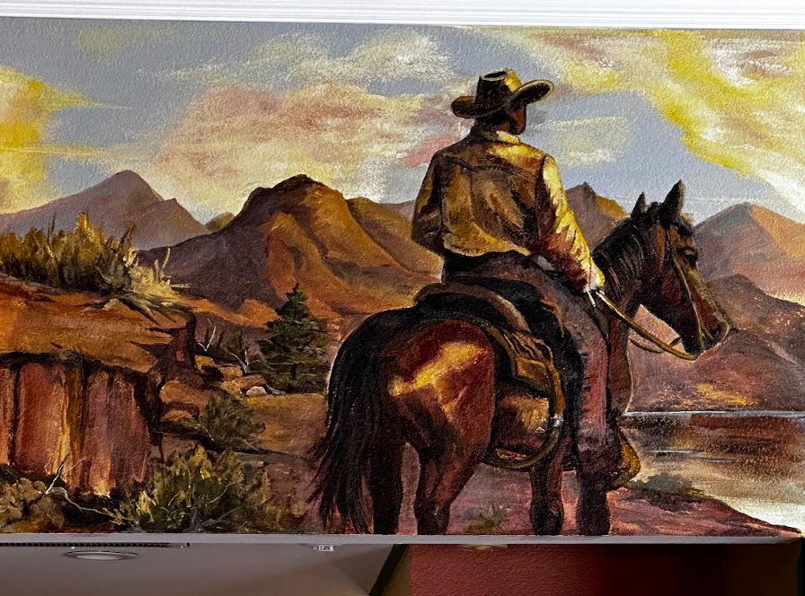 Cowboy on horseback overlooking desert mountains at sunset, with warm golden and purple tones.