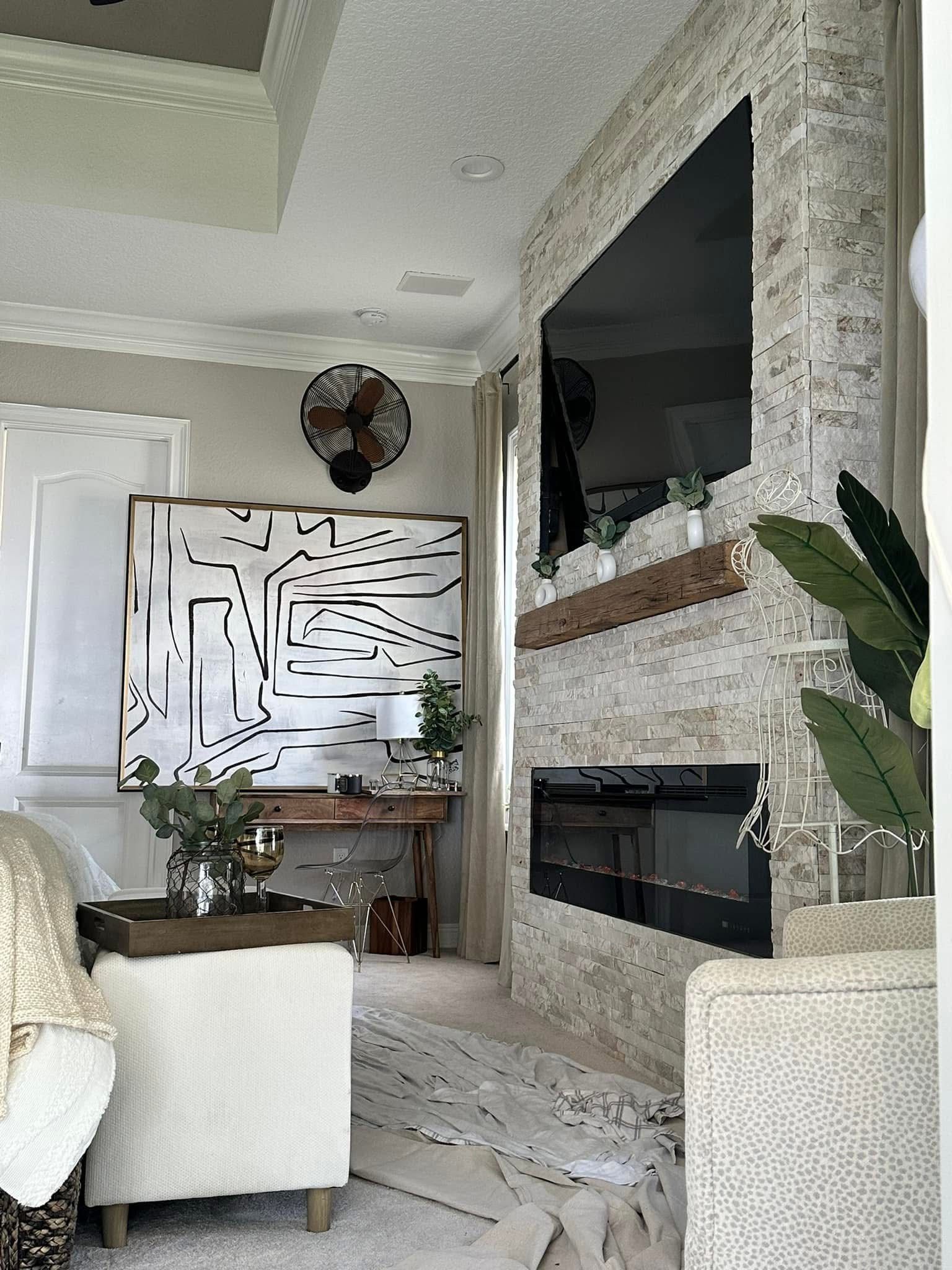 Bright living room with stone fireplace, large TV, white chairs, and modern abstract wall art