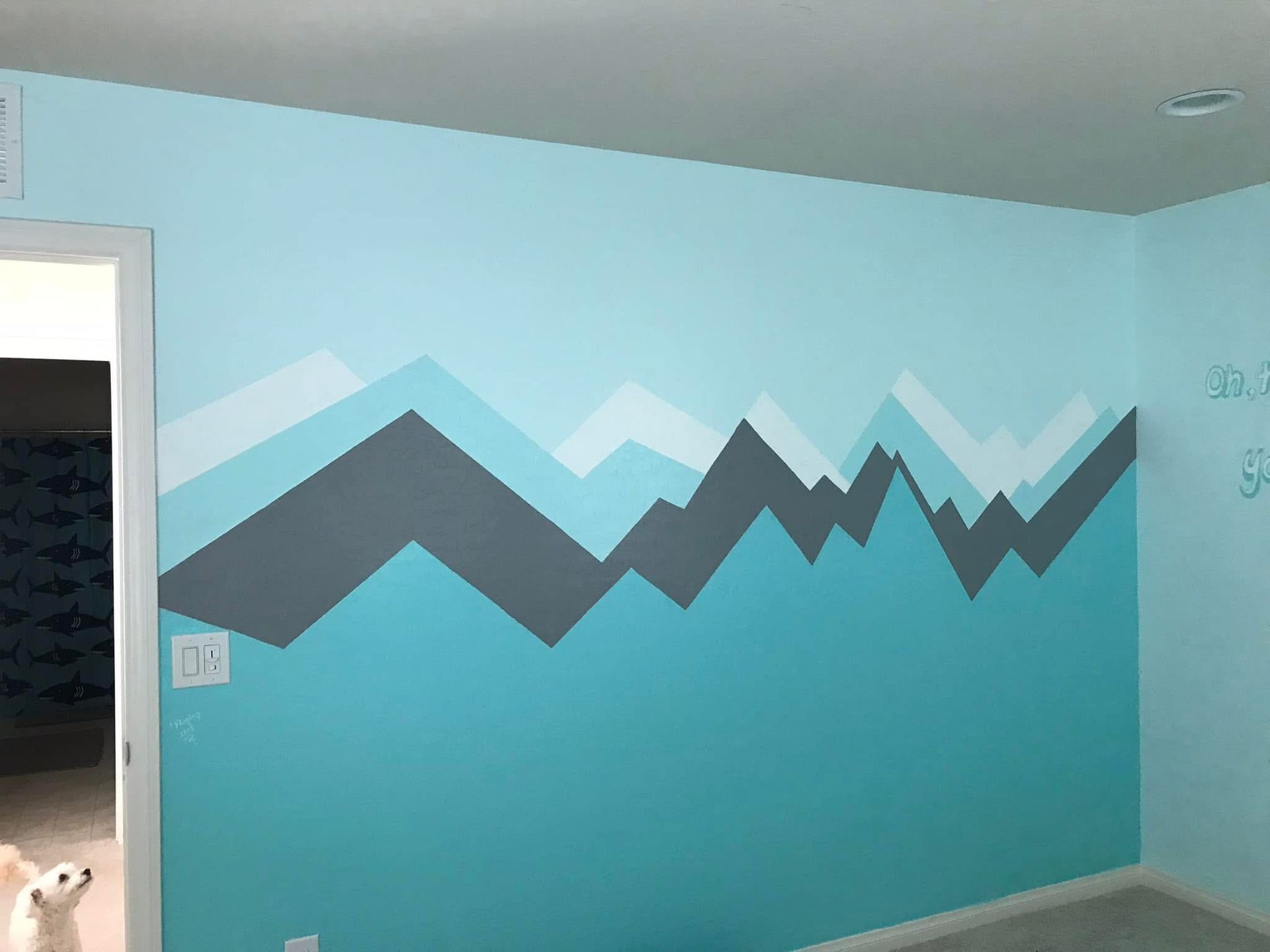 A turquoise room wall with a gray and white mountain mural across the center