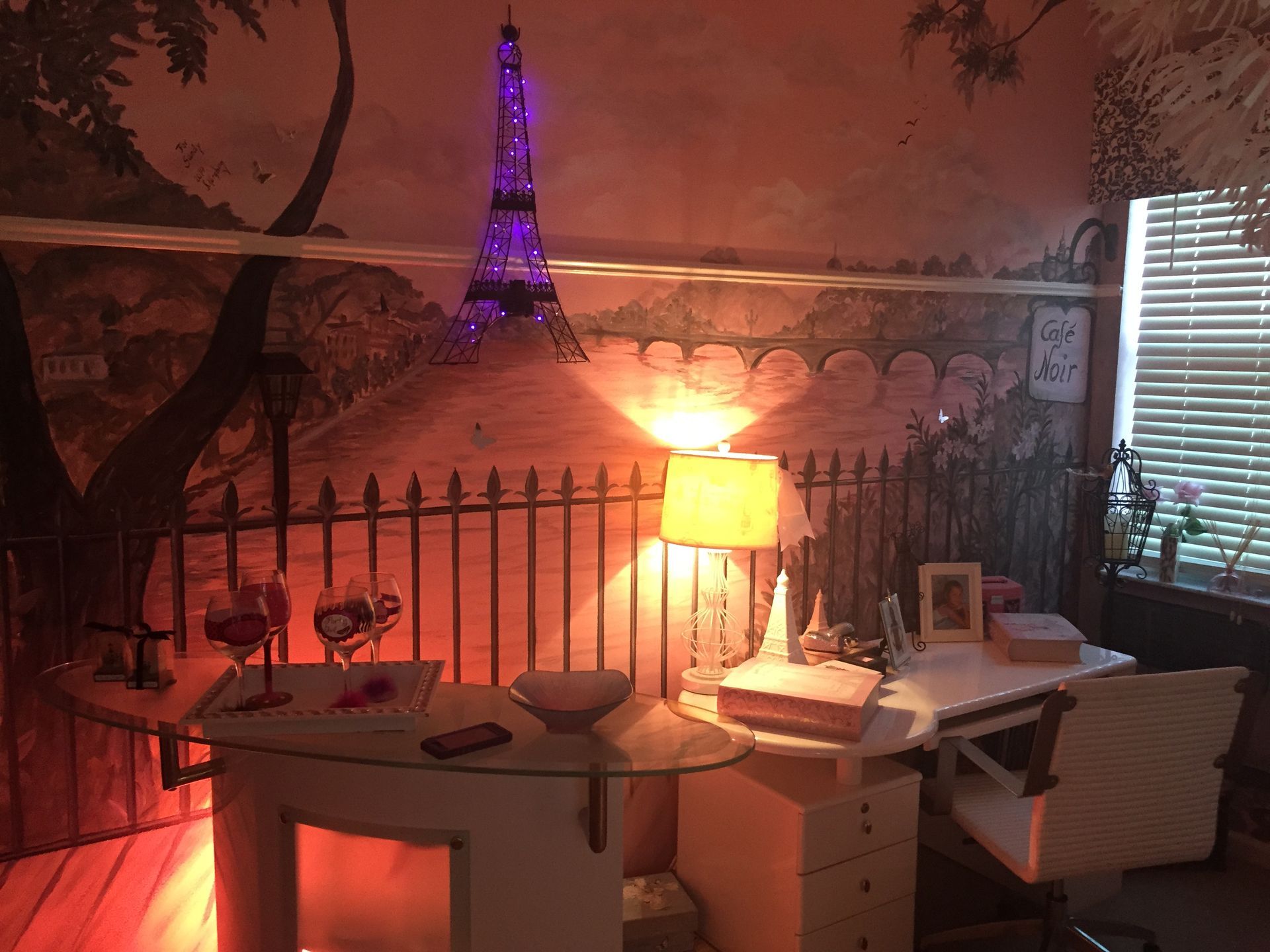 Cozy room with Eiffel Tower mural, warm lamp glow, and a desk by a window with blinds.