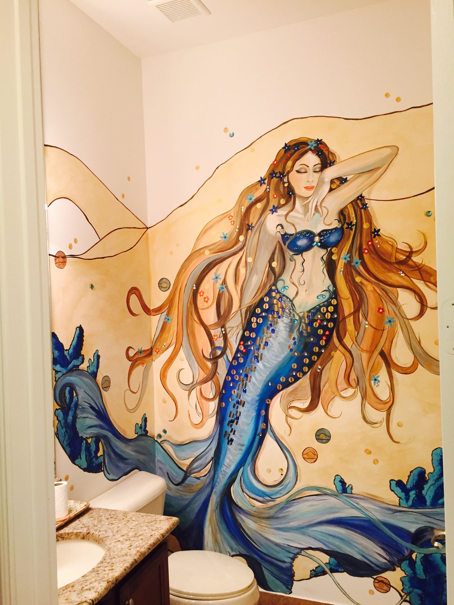 Mermaid mural with a blue tail and long flowing hair painted on a bathroom wall.